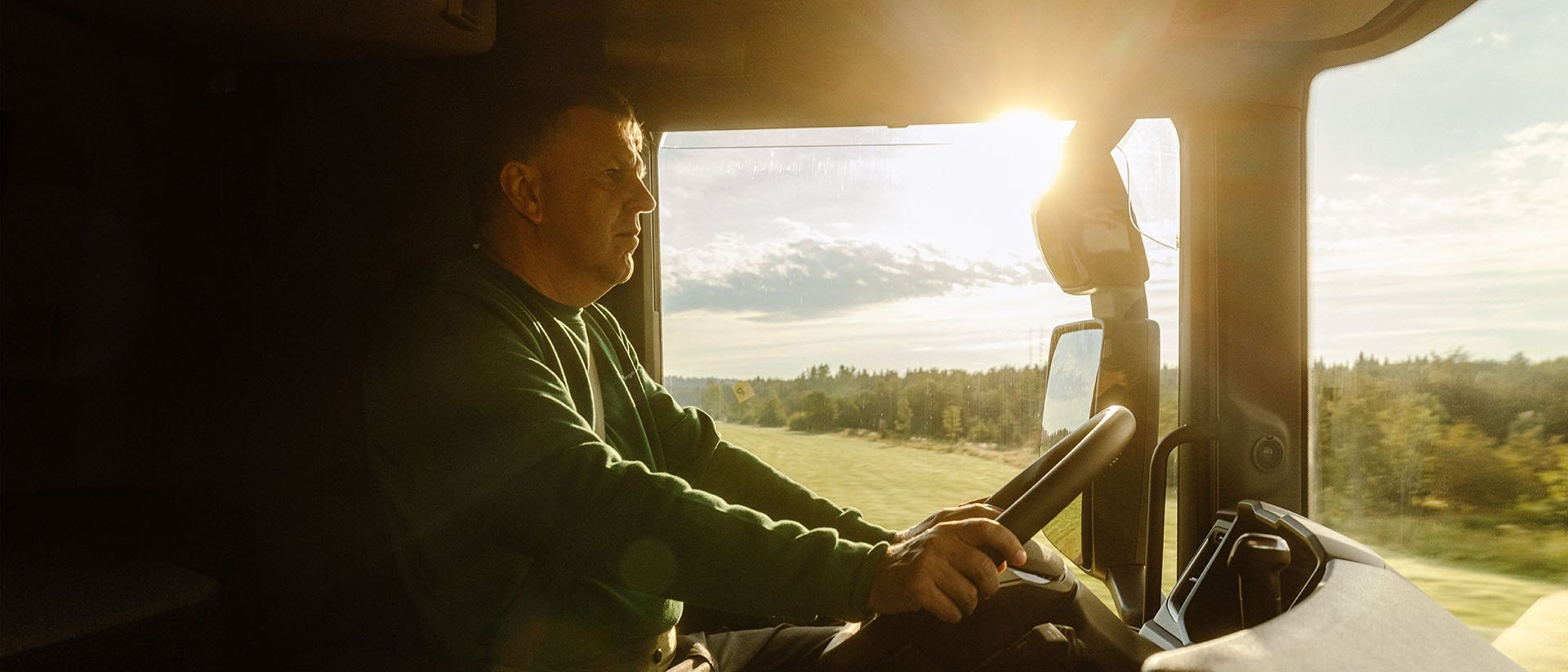 Ein LKW-Fahrer von Swiss Post Cargo steuert sein Fahrzeug auf einer Direktfahrt durch eine sonnige Landschaft.