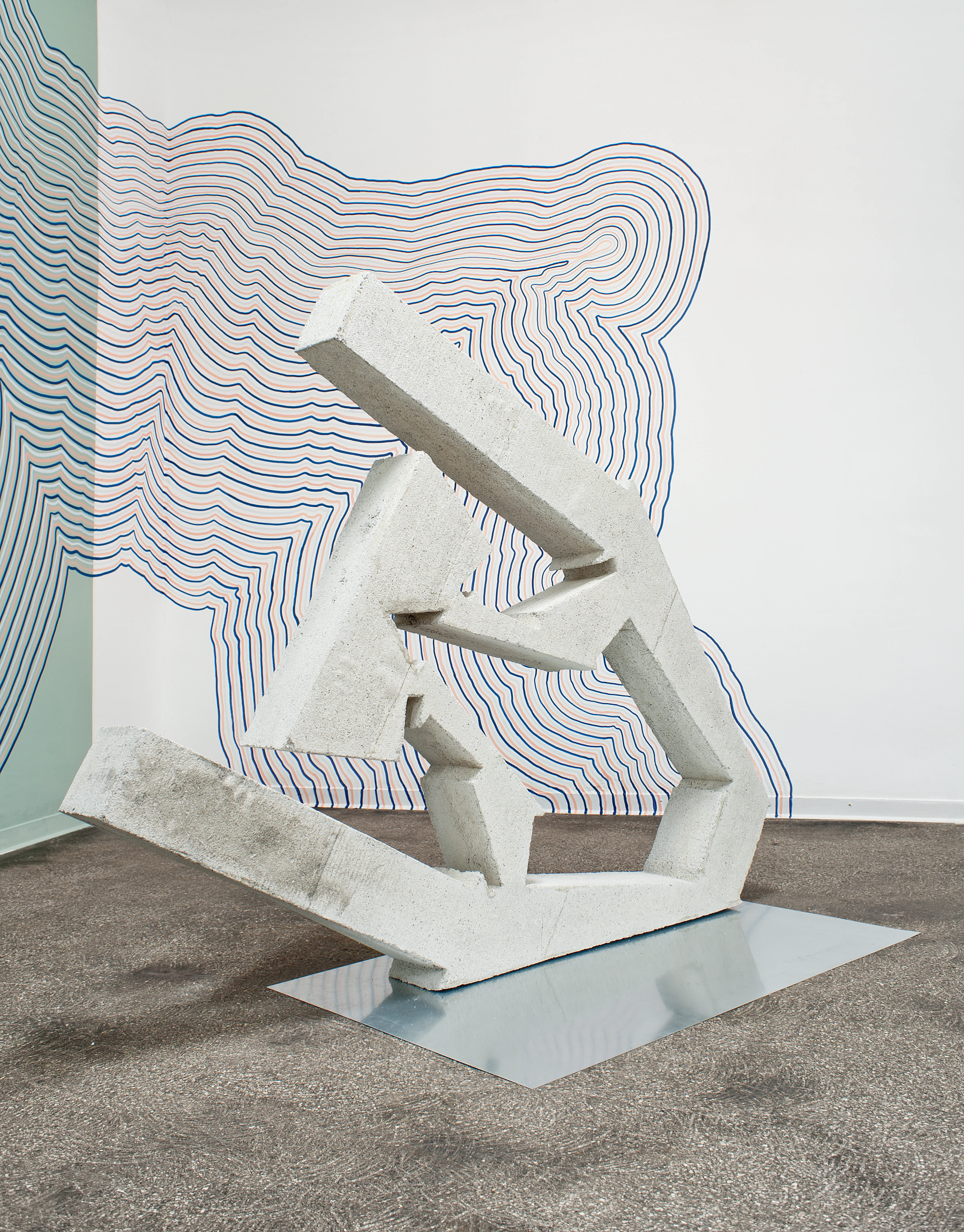 Eine abstrakte, steinerne Skulptur vor einer gemusterten Wand.