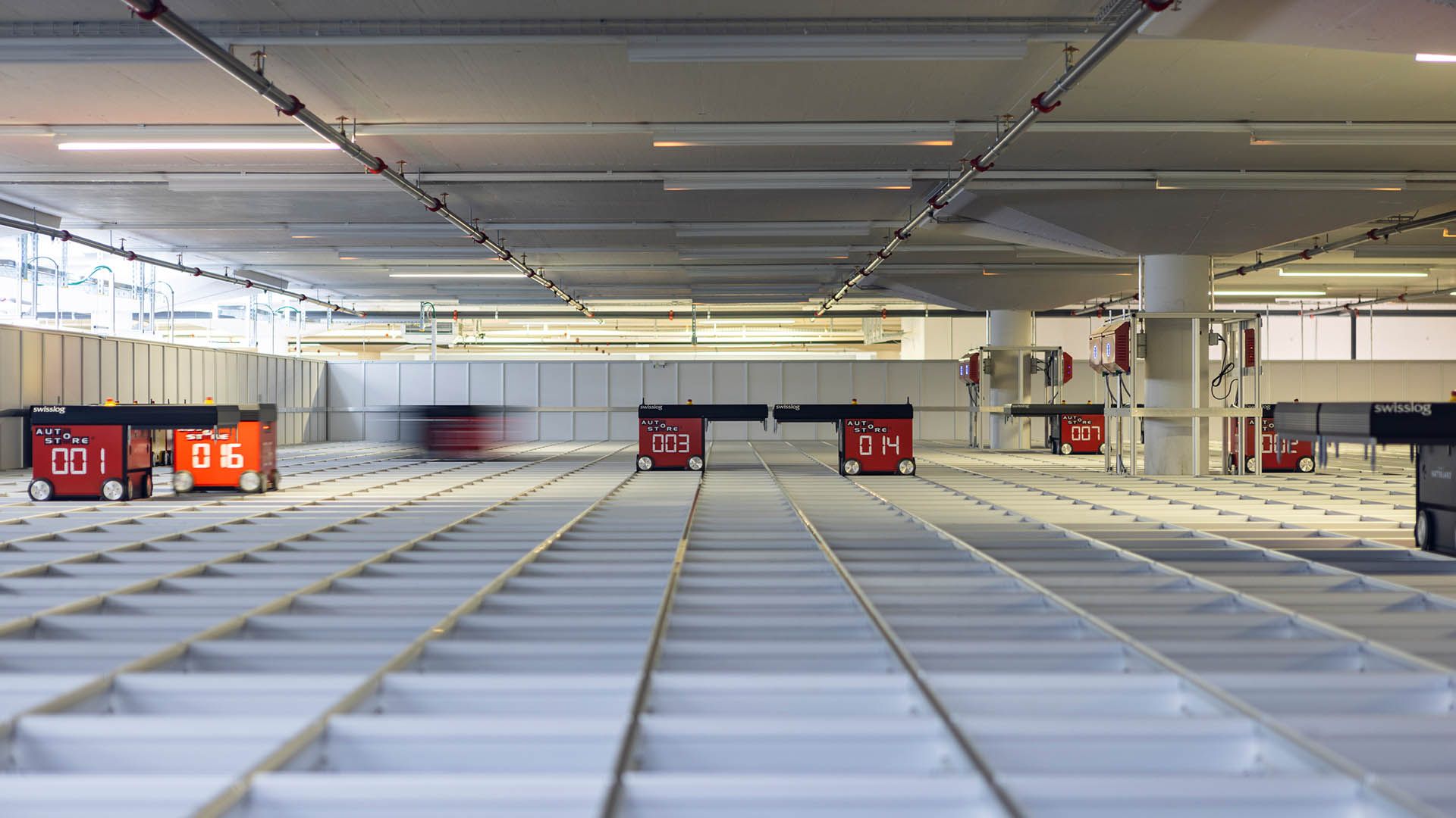 Automatisiertes Lagersystem mit autonomen Robotern auf einem Raster aus Lagerbehältern. Die Roboter von Swisslog bewegen sich präzise auf Schienen, um Waren effizient ein- und auszulagern.