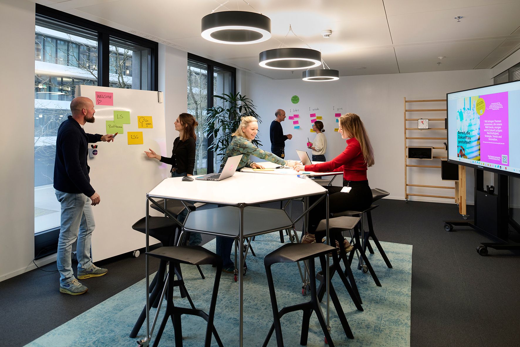 Eine Gruppe von Menschen arbeitet in einem modernen Büro mit Tafeln und Laptops.
