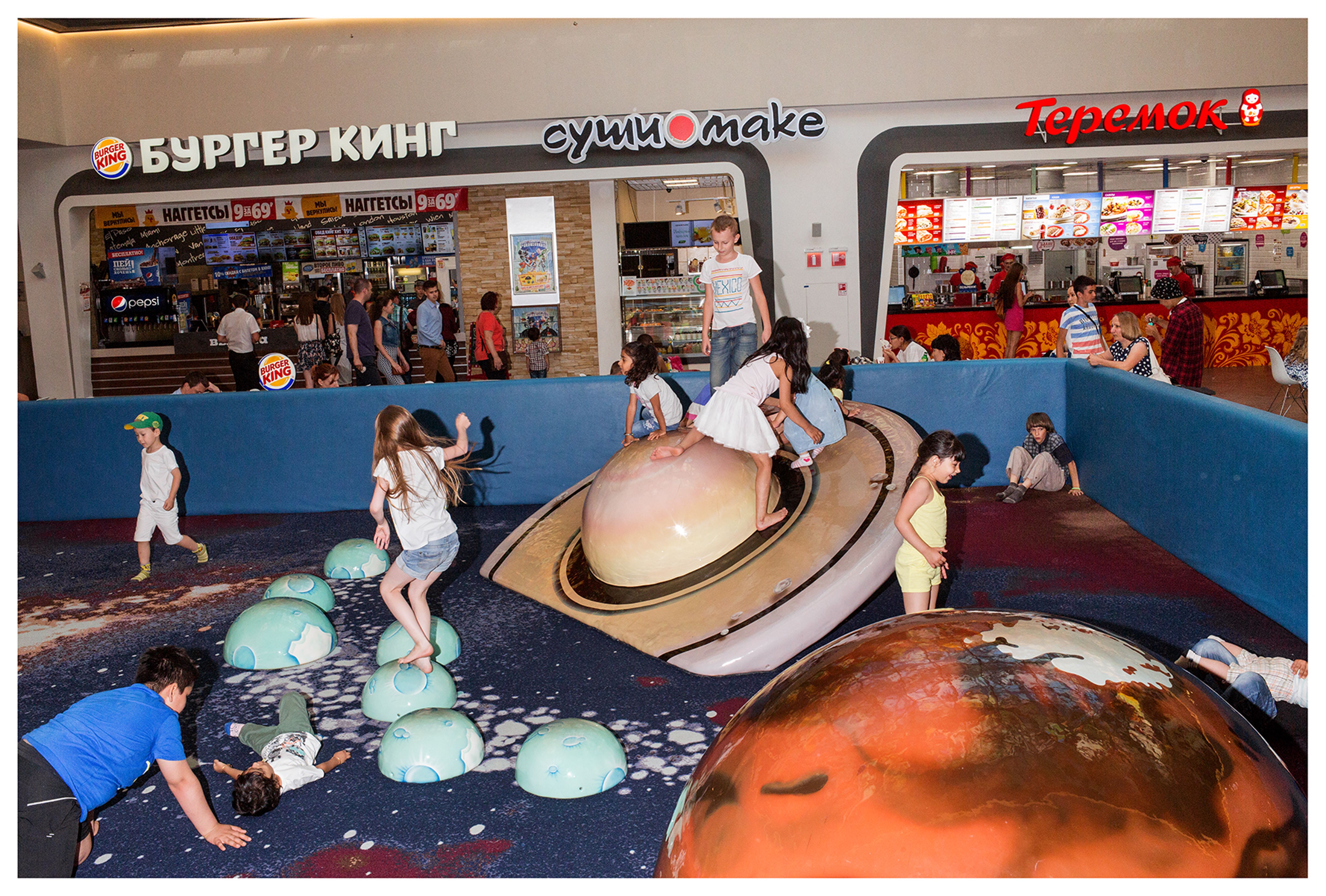 Children playing on planetary structures in a bright shopping center.