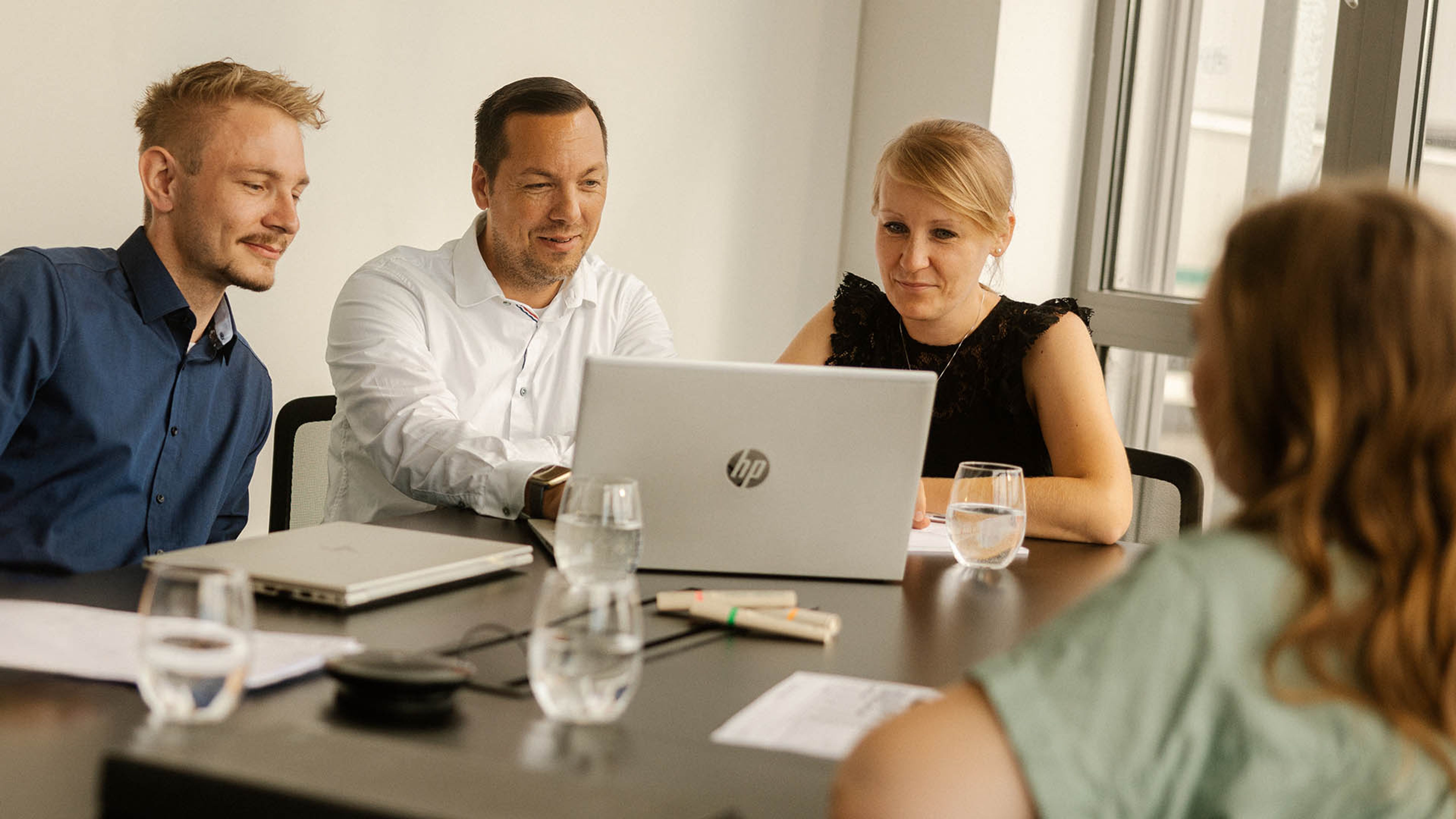 A meeting with four employees, three of whom are looking at a laptop together.