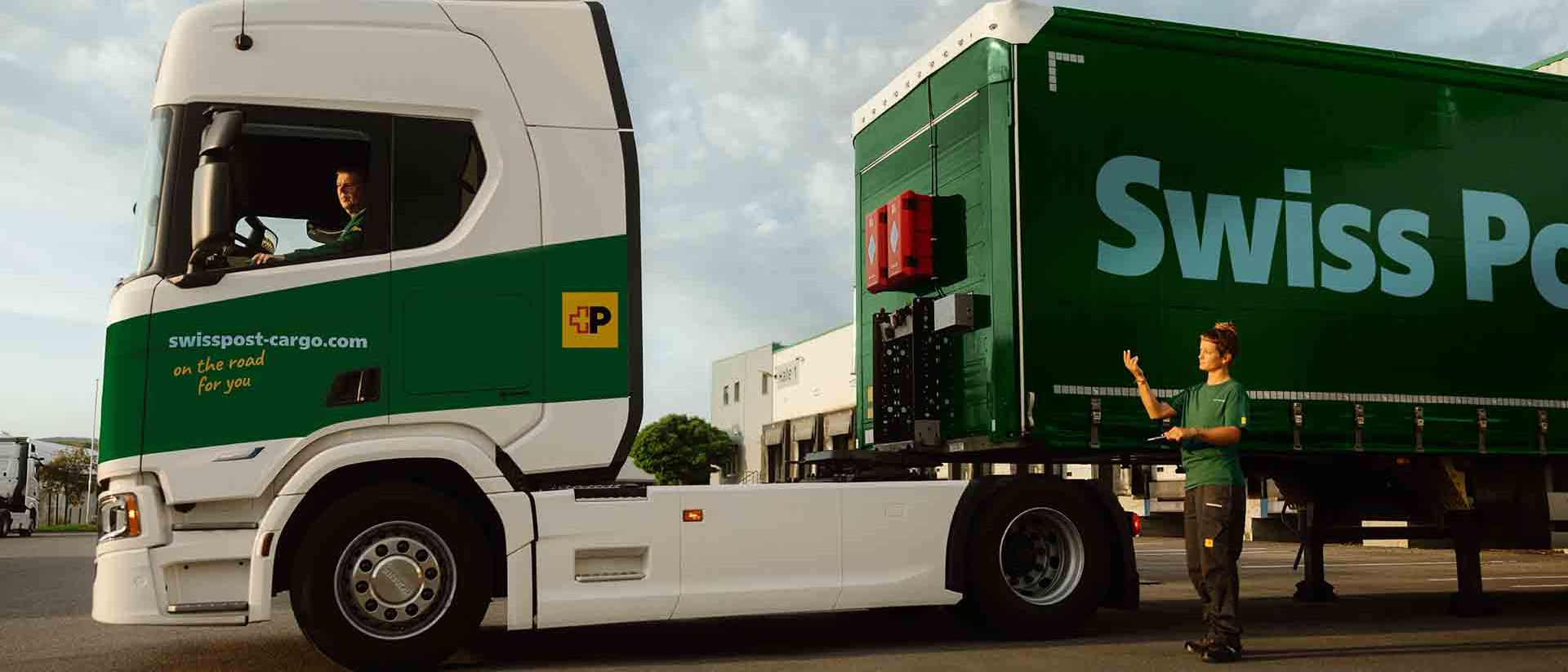 Un chauffeur de camion Swiss Post Cargo attelle une remorque, assisté par une collègue.