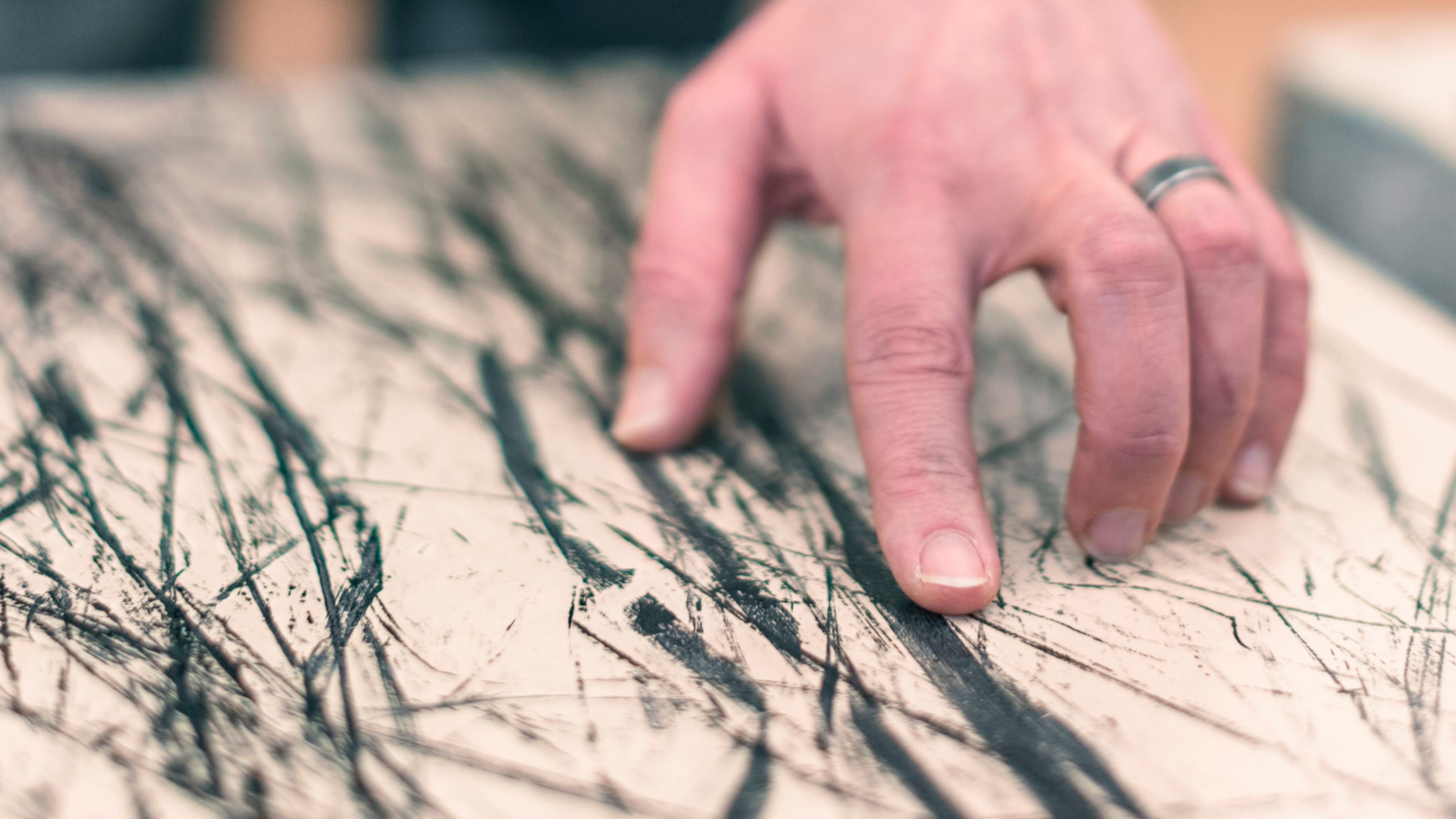 Eine Hand berührt eine mit schwarzen Linien versehene Oberfläche.