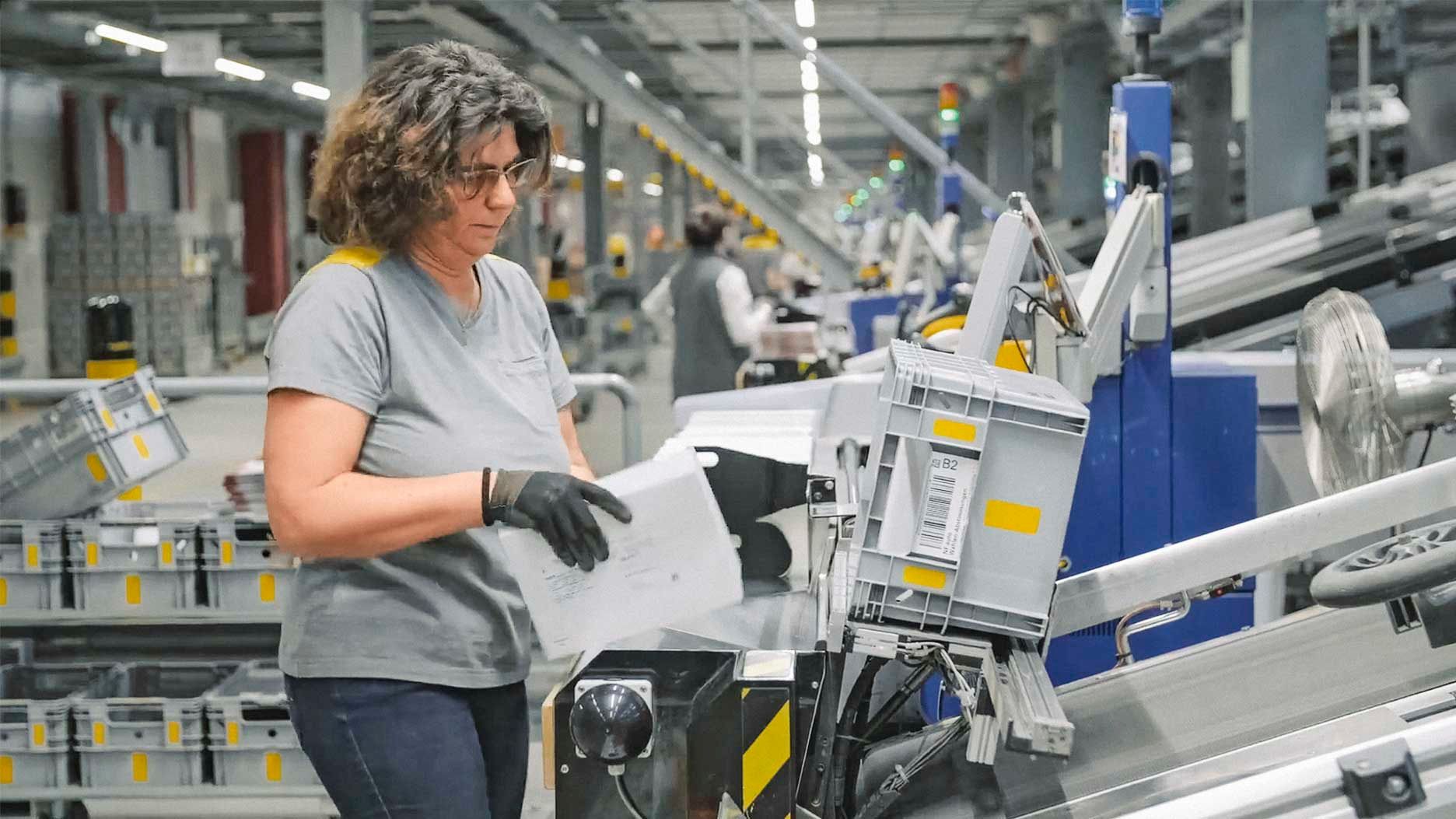 Frau beim entnehmen von Briefen aus einer Briefsortiermaschine