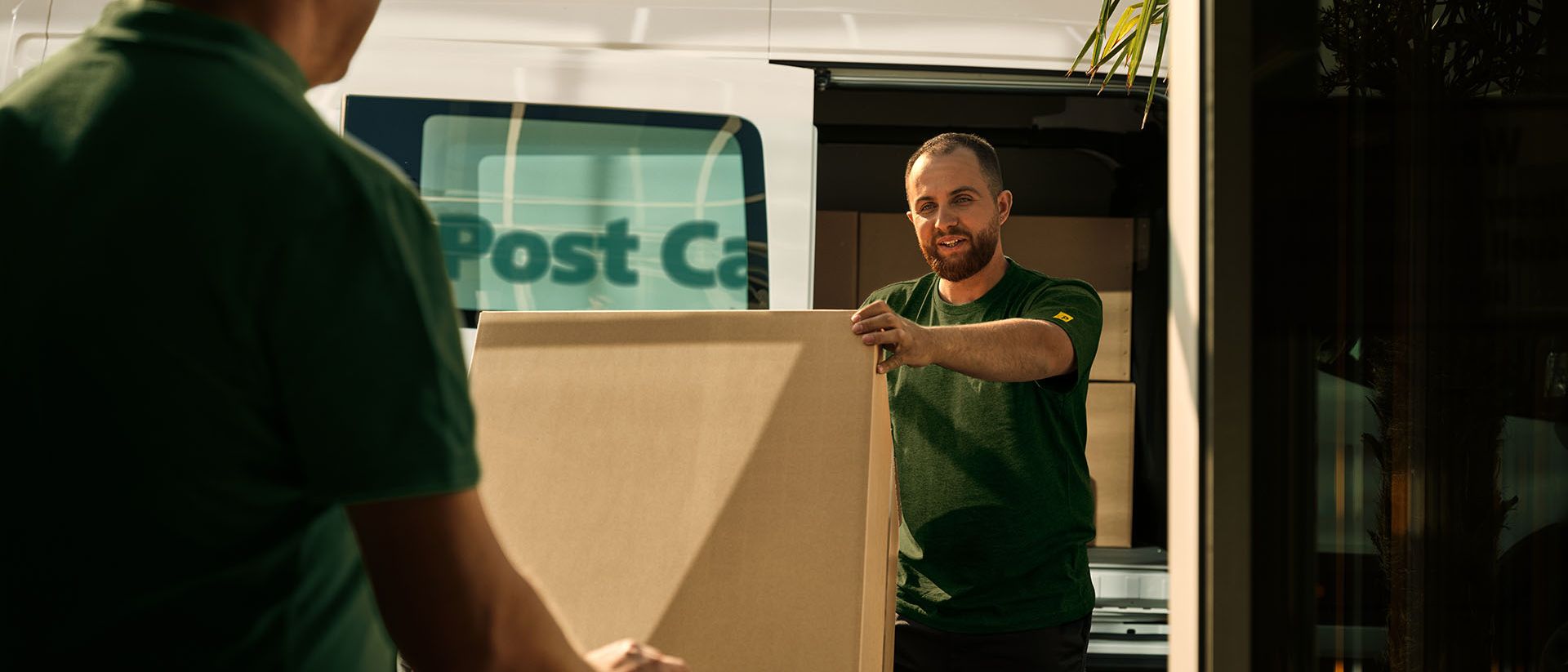 Deux personnes employées de Swiss Post Cargo déchargent une livraison encombrante d’un véhicule.