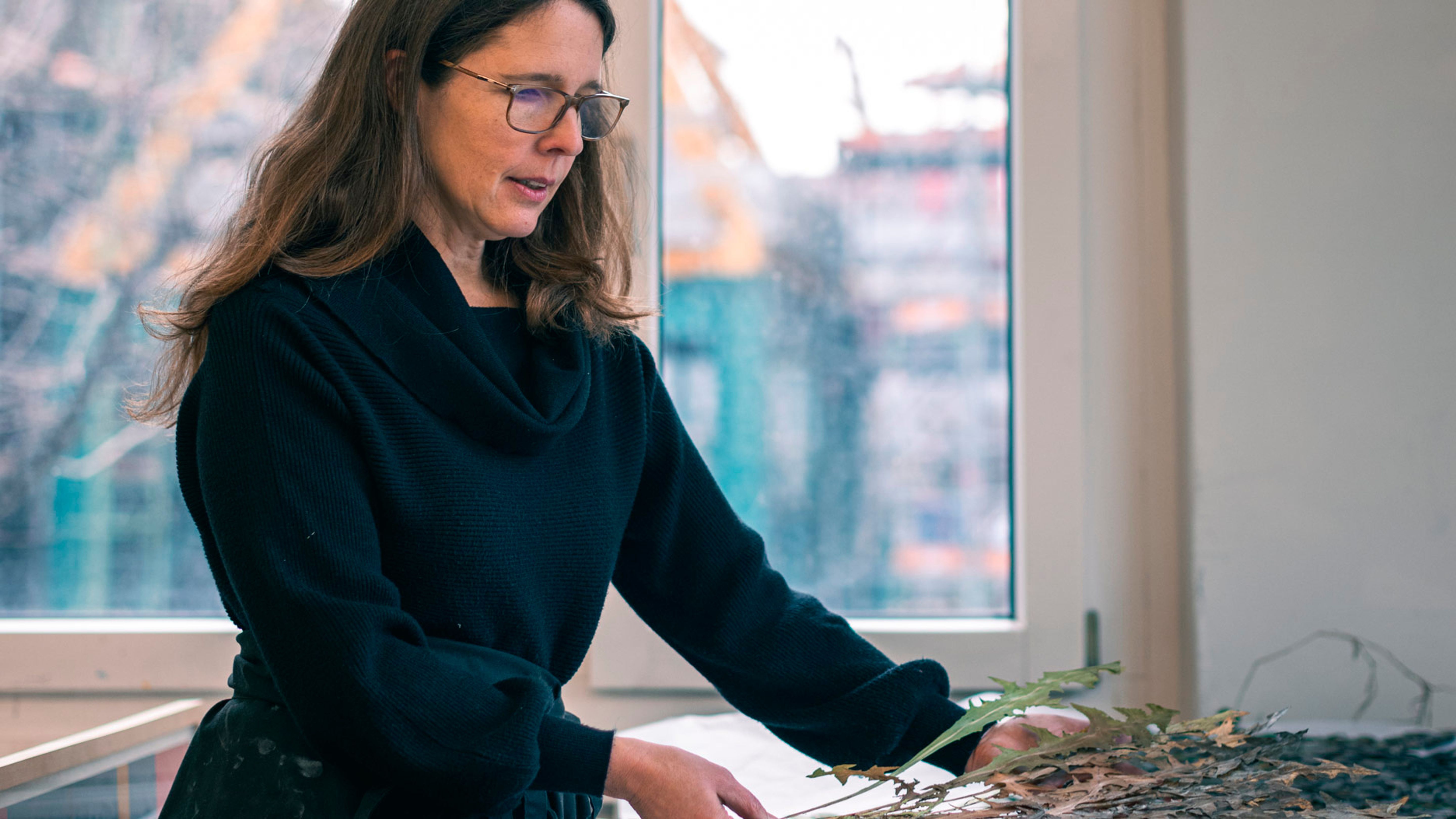 Eine Frau steht vor einem Fenster und arbeitet mit Laub.