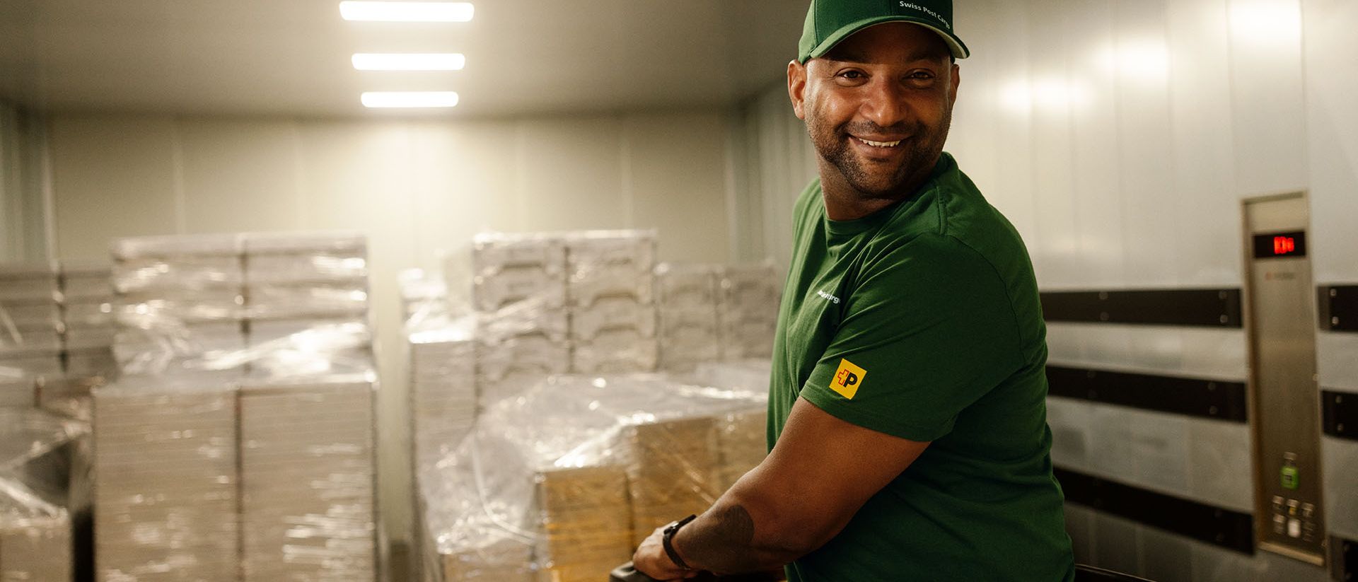 A Swiss Post Cargo warehouse worker moves general cargo on a pallet jack into an elevator.
