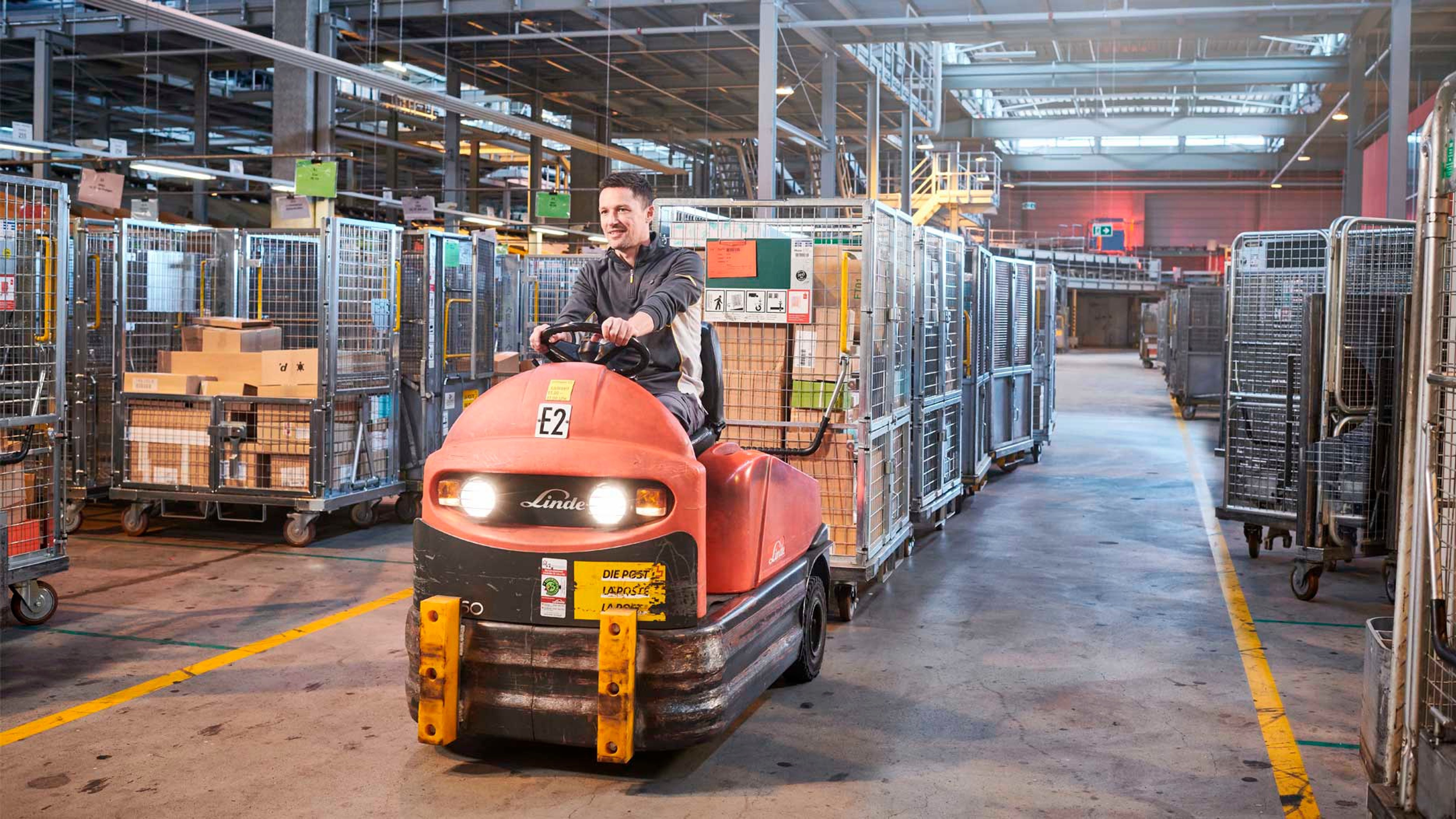 Ein man auf einem elektrischen Zugfahrzeug transportiert mehrer angehängte Rollbehälter mit Paketen