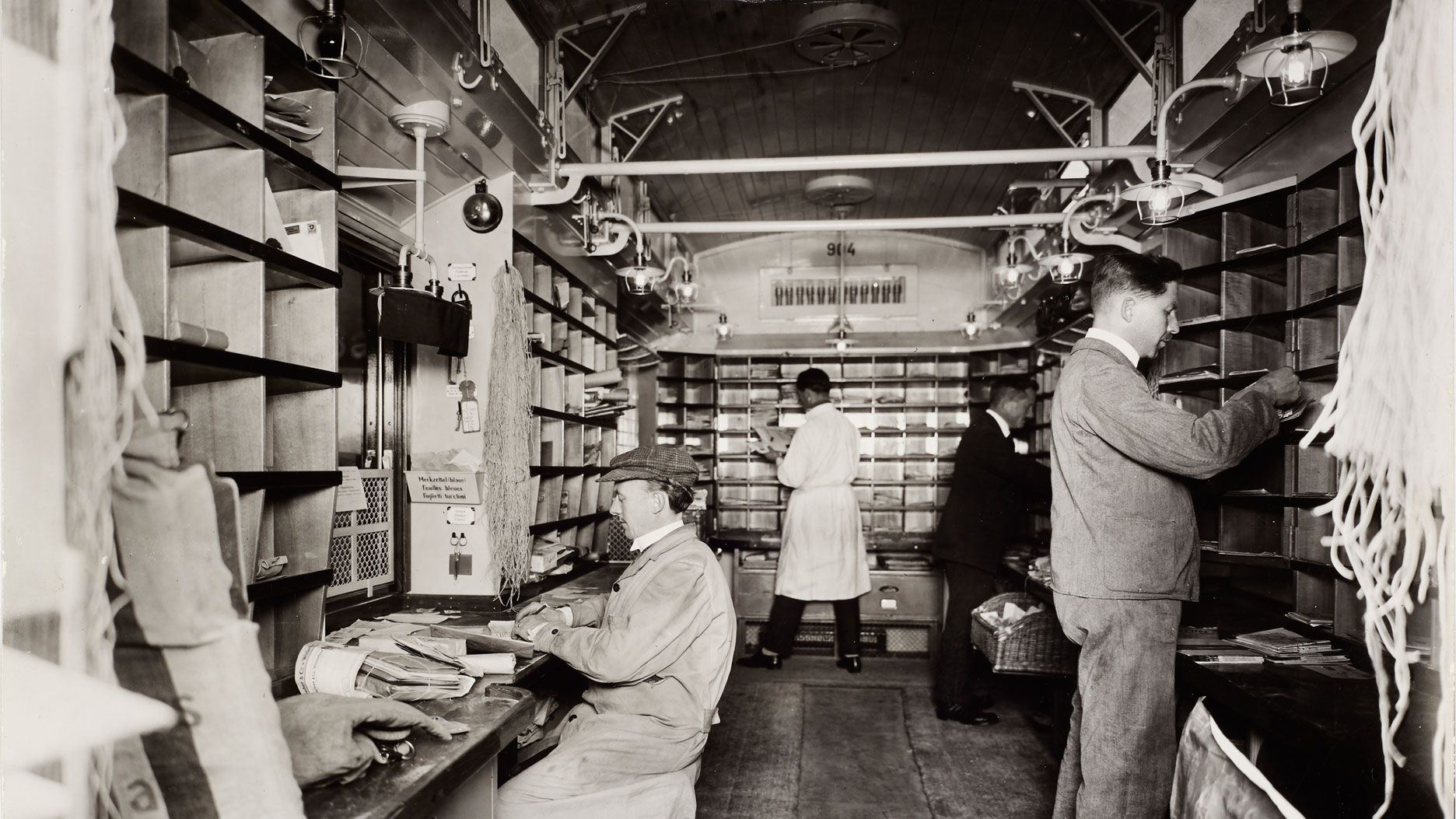 Bahnpöstler bei der Unterwegssortierung im Büroraum des Bahnpostwagens auf der Strecke Basel–Belfort 1926. Quelle: Museum für Kommunikation