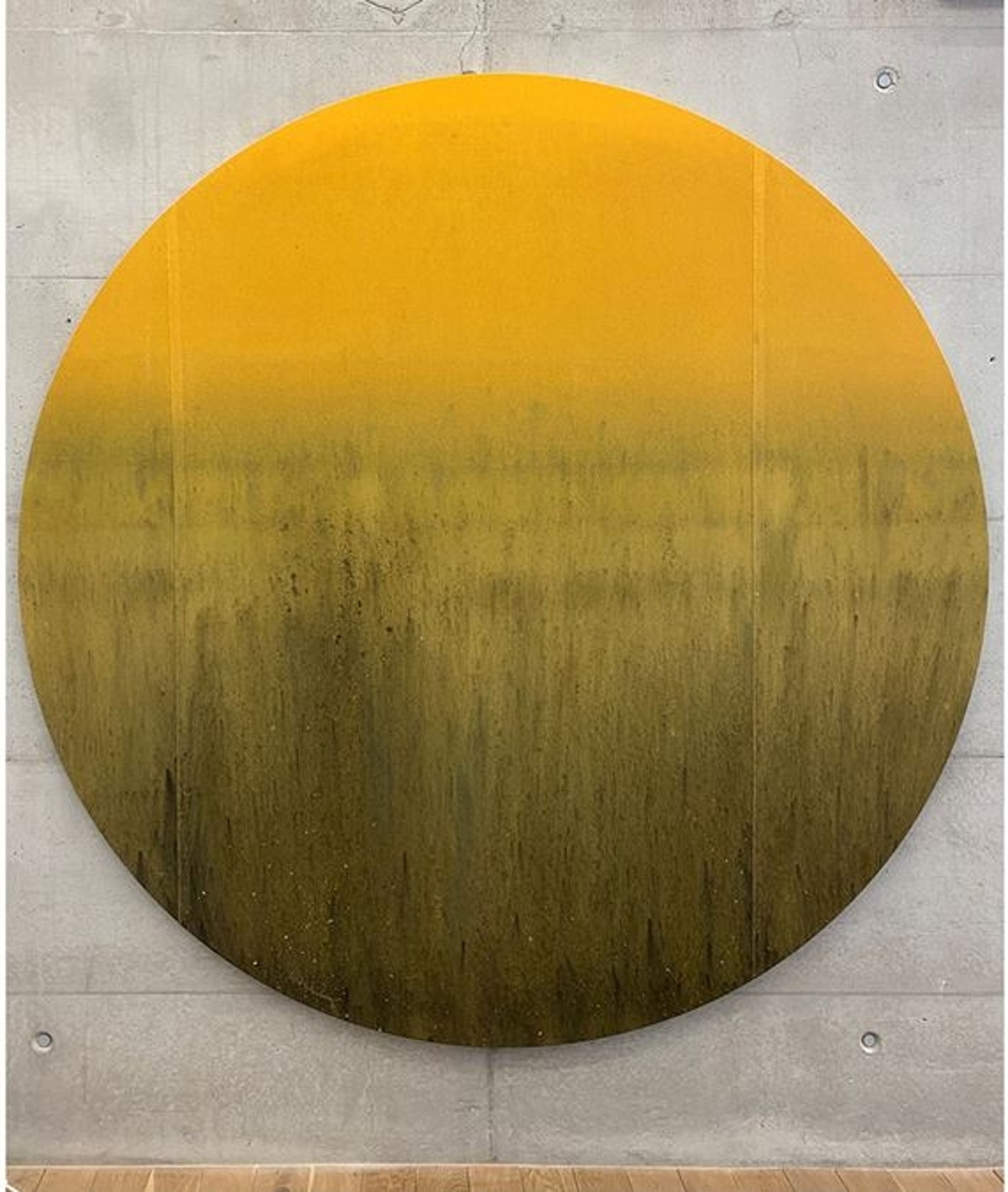 A round work of art with a yellow-to-green colour gradient hangs on a concrete wall.