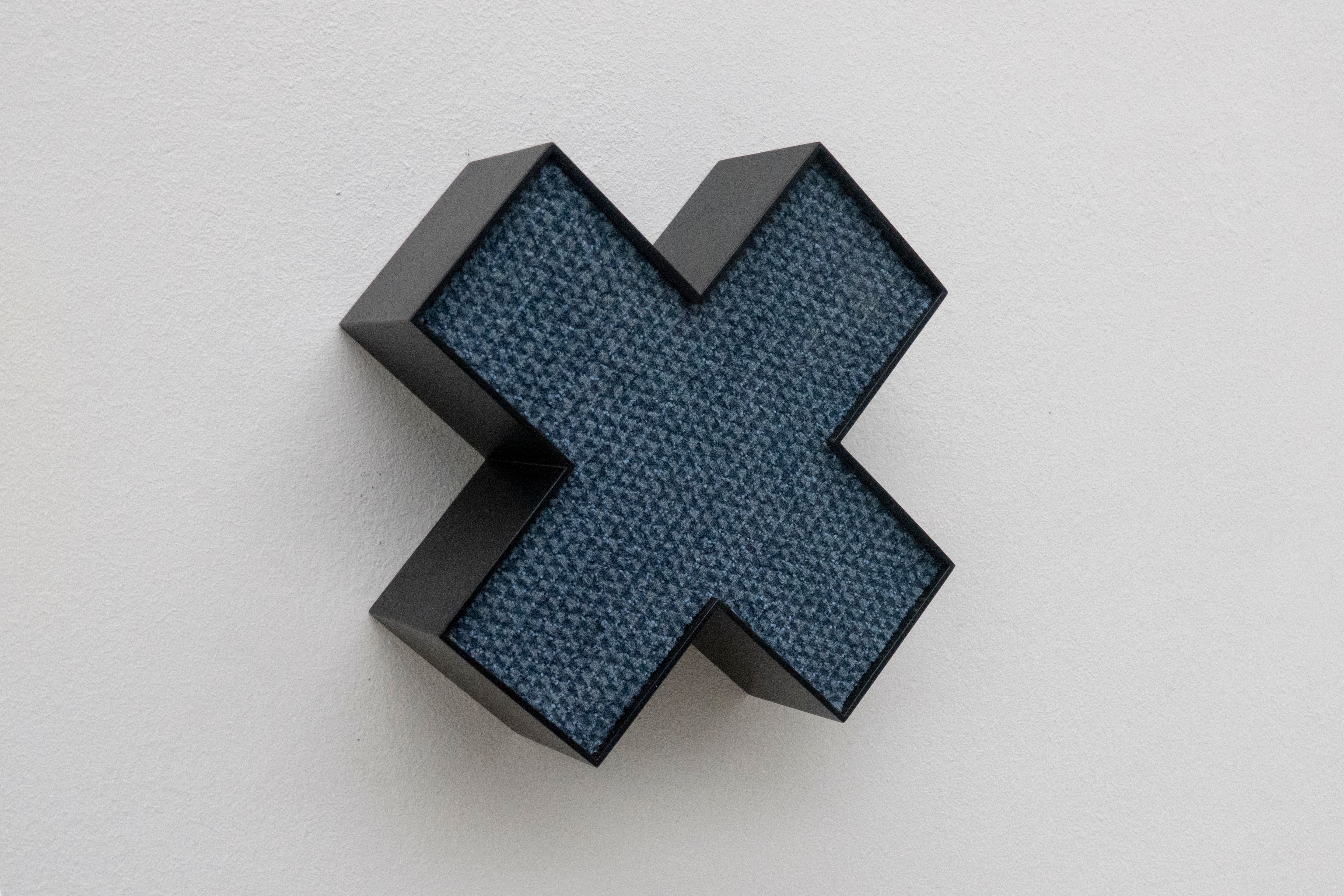X-förmiges Objekt mit blauem Inneren an einer weissen Wand.