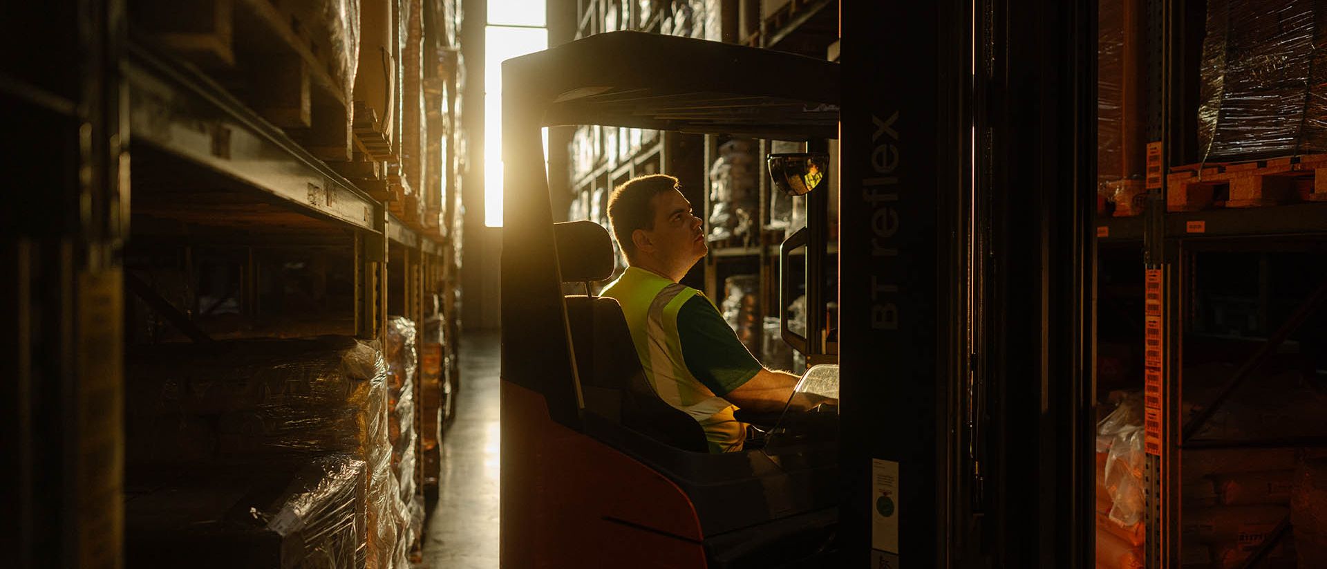 Dans un entrepôt, un employé de Swiss Post Cargo conduit un chariot élévateur entre les étagères.