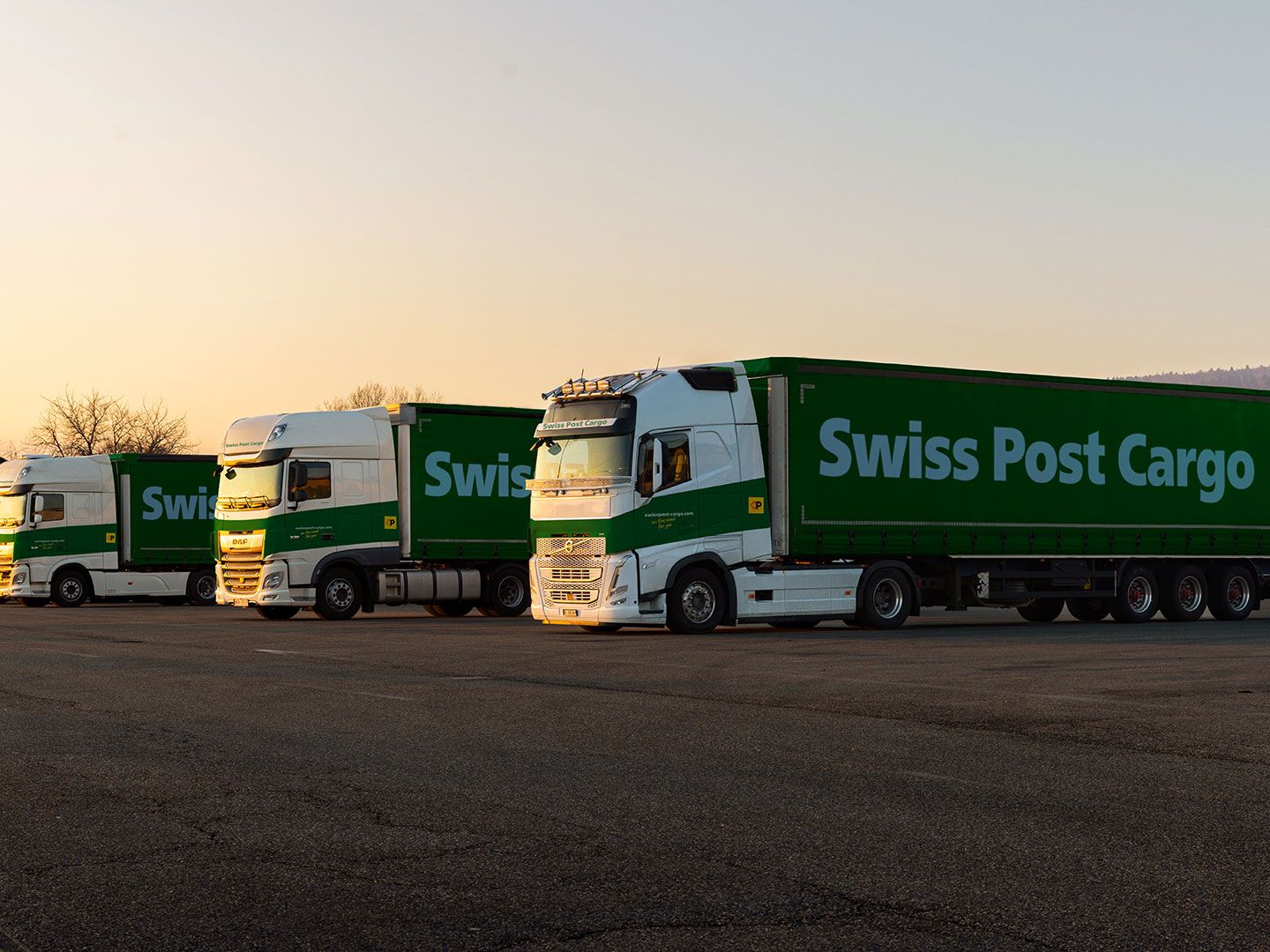 Swiss Post Cargo lorries stand in front of the logistics center at dusk.