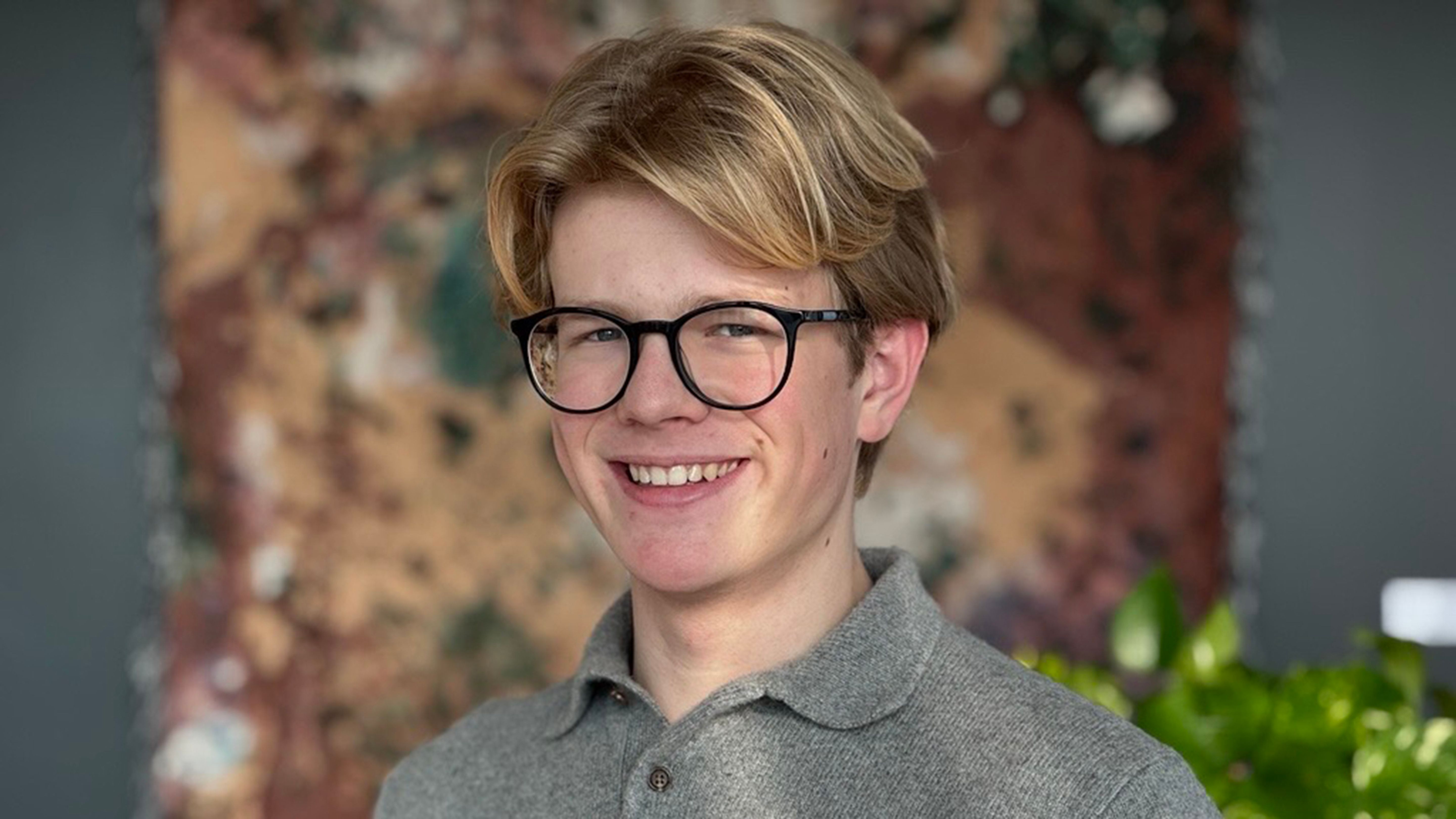 Portrait d’un garçon blond souriant à la caméra.
