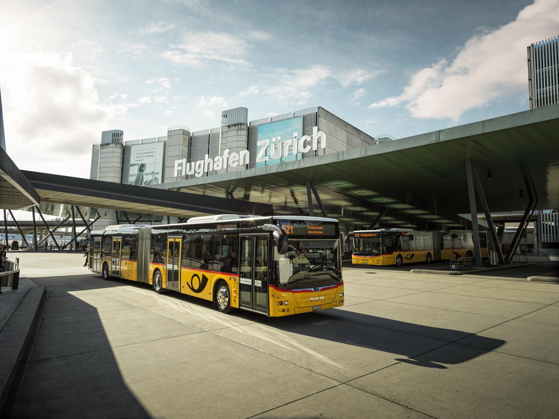 A yellow bus in front of the Zurich airport terminal in sunny weather.