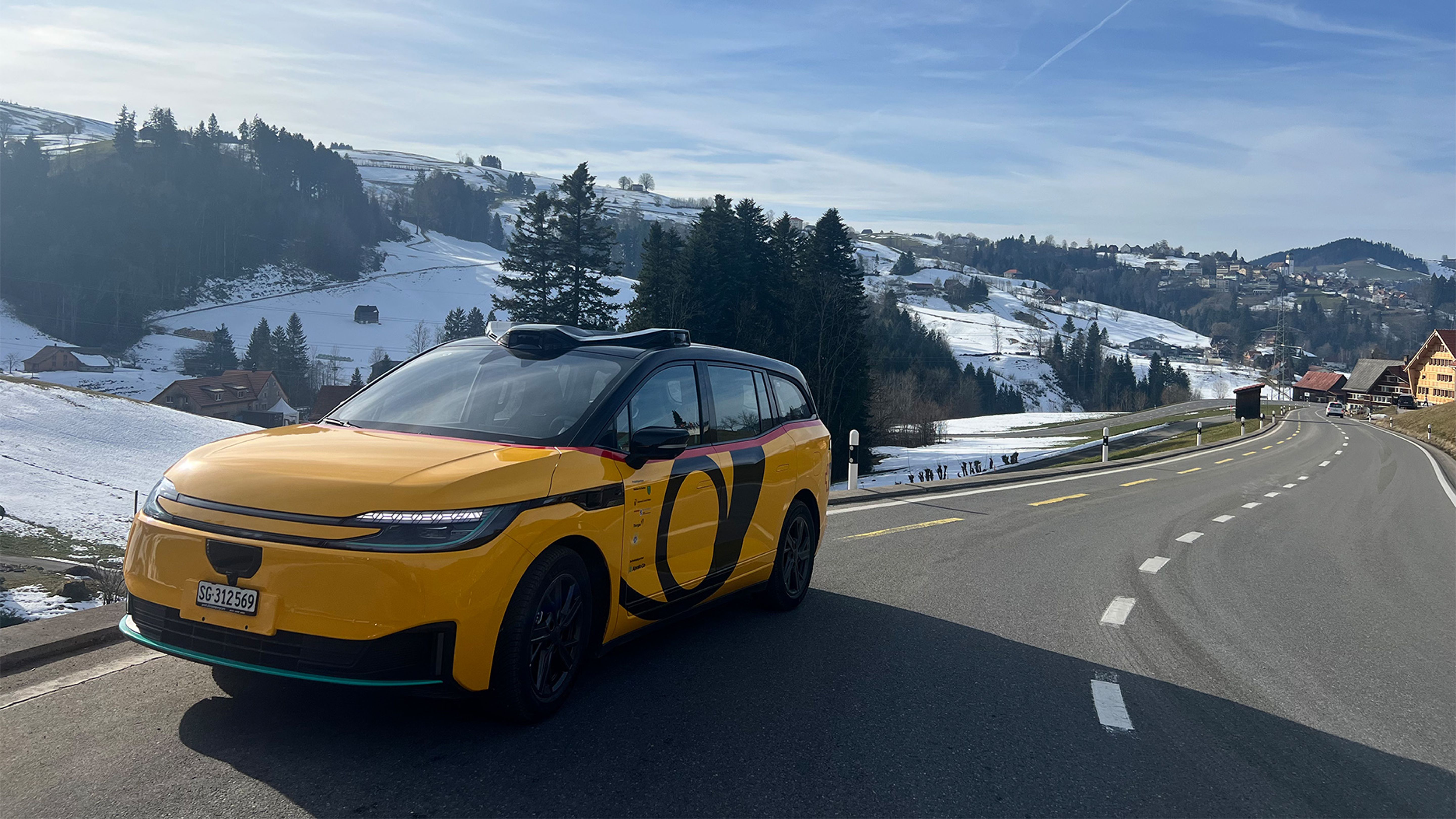 A yellow vehicle stands on a street in a wintry rural area.