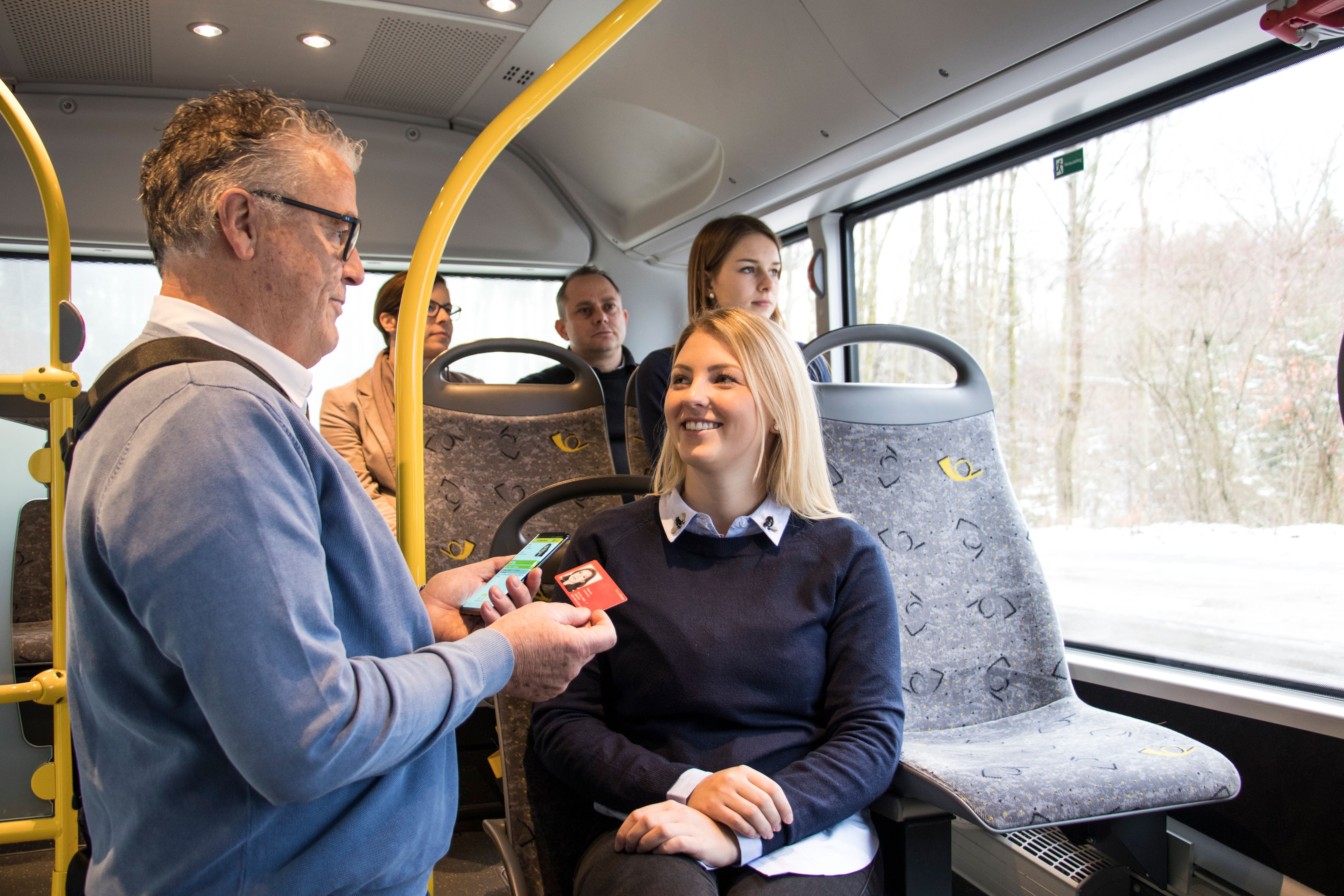 A man shows a woman a map in an interior bus with a wintry landscape.
