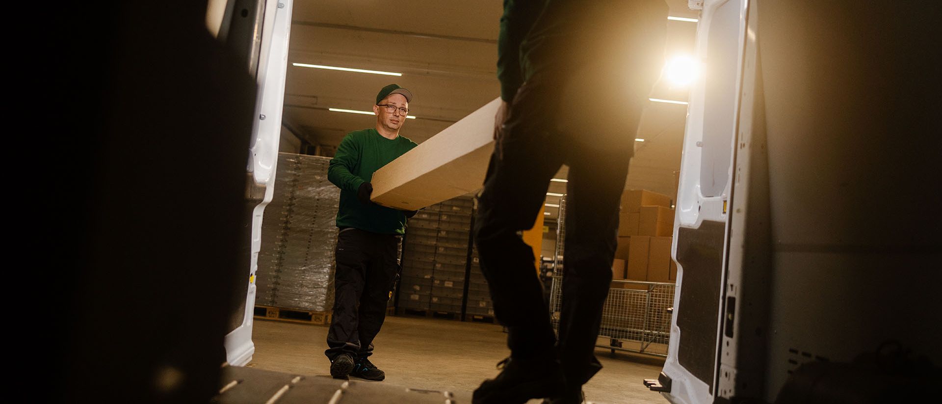 Two Swiss Post Cargo employees load spare parts into a service vehicle at night.