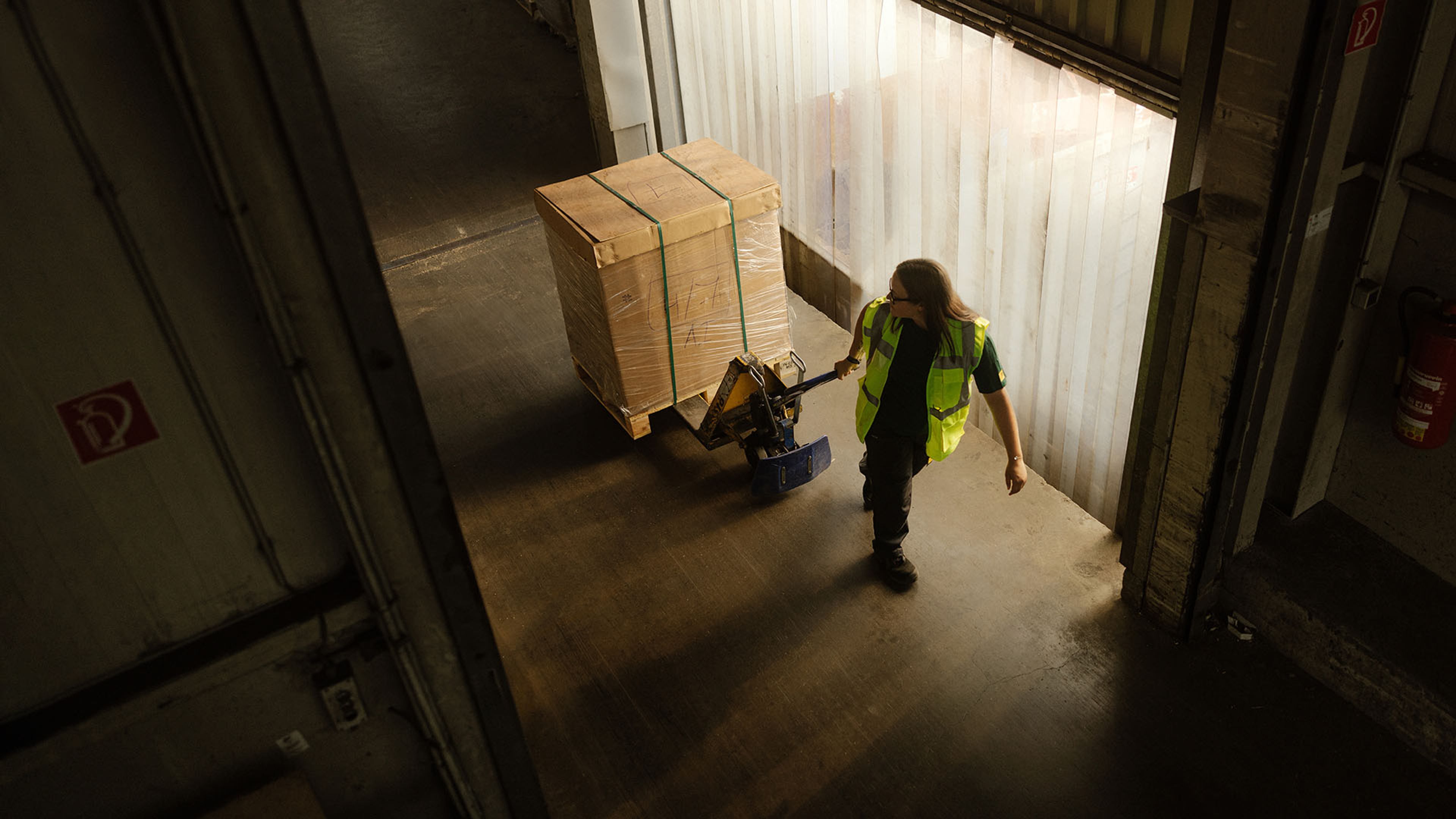 Ein Lagerarbeiter von Swiss Post Cargo fährt Stückgut auf einem Hubwagen in einen Fahrstuhl.