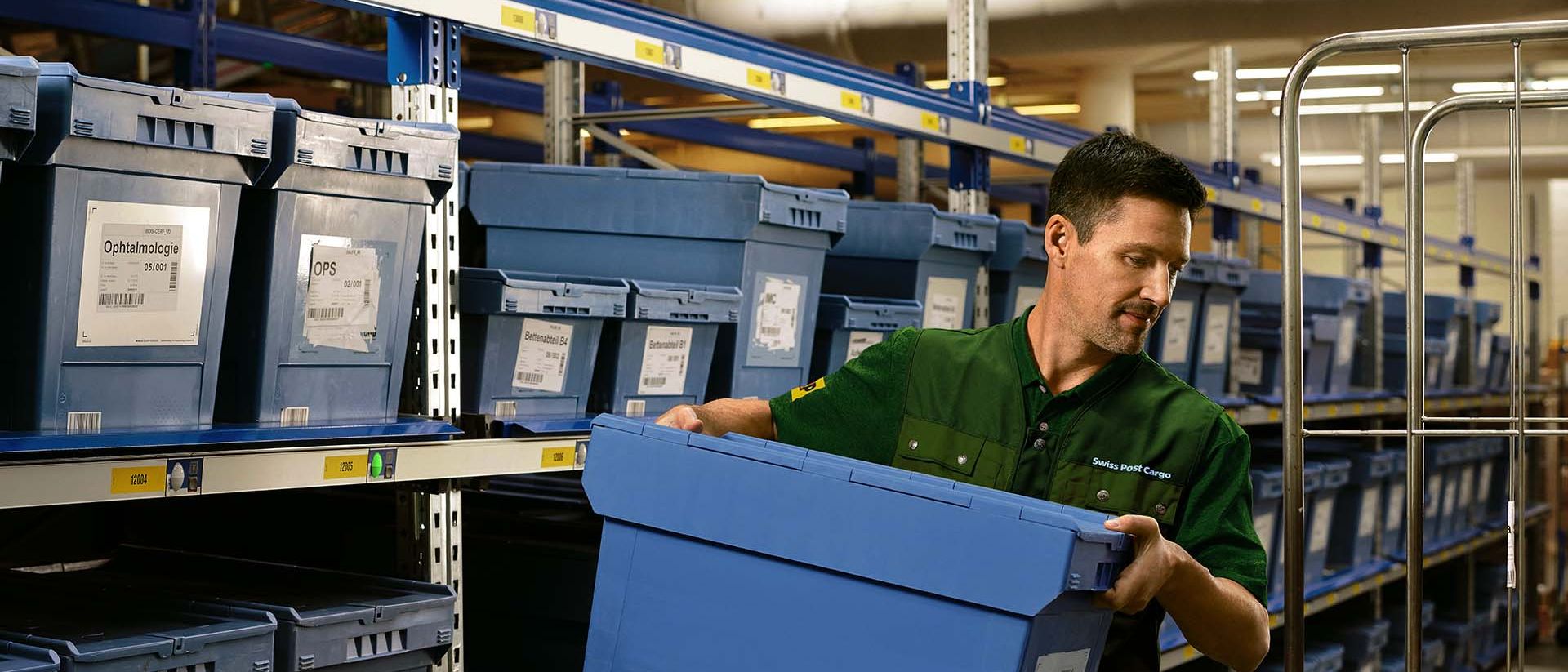 Ein Lagermitarbeiter lädt eine Box mit Pharma-Waren von einem Regal auf einen Rollwagen.
