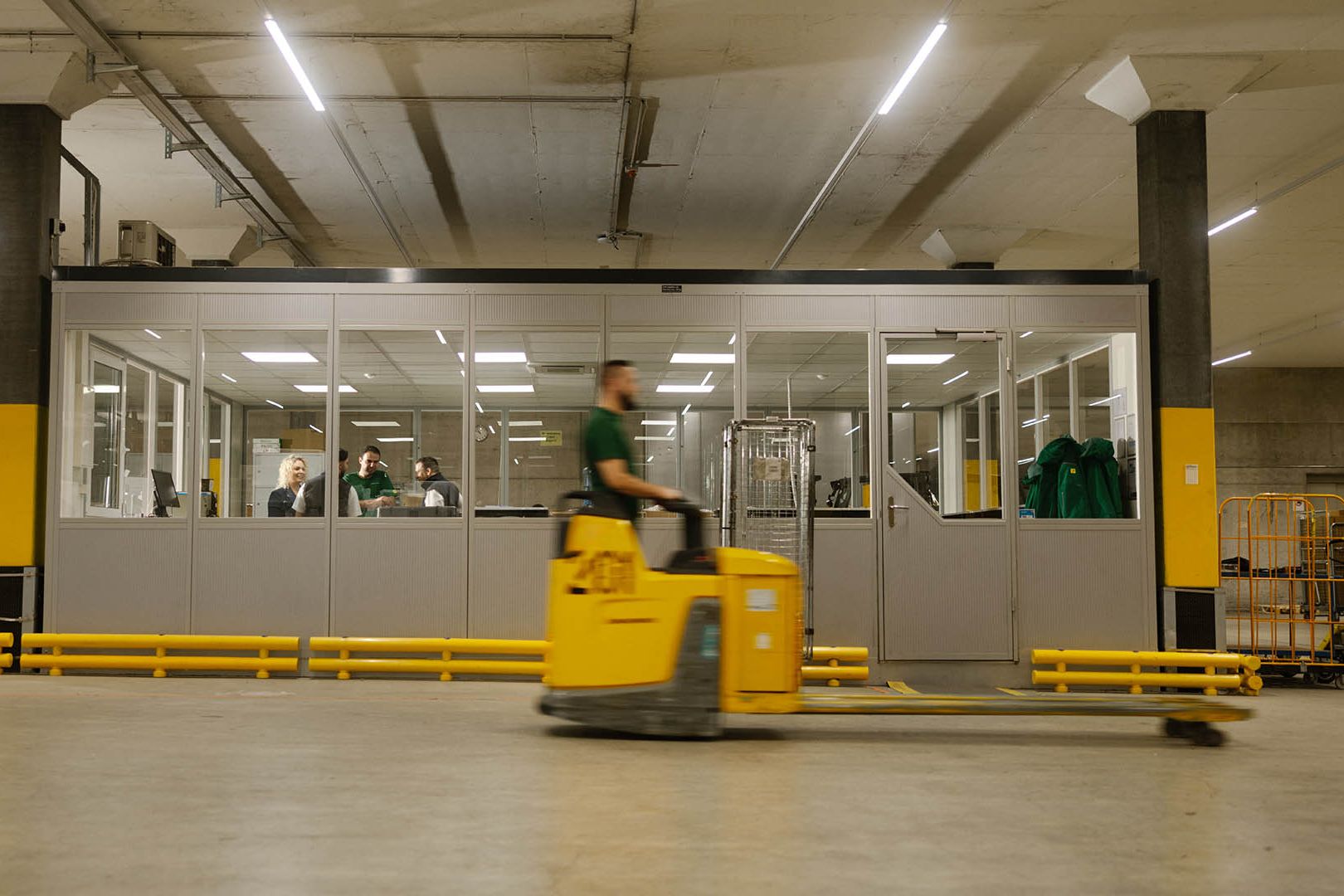 In einer Lagerhalle fährt ein Swiss Post Cargo Mitarbeiter auf einem Hubwagen an einem verglasten Raum vorbei.