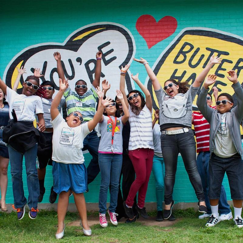 Group of kids jumping in the air in front of the United Way for Greater Austin's Butter Half mural.