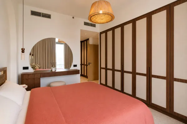 Warm minimalist master bedroom in Dubai hills with a built-in wardrobe, floating makeup station and earthy terracotta tones