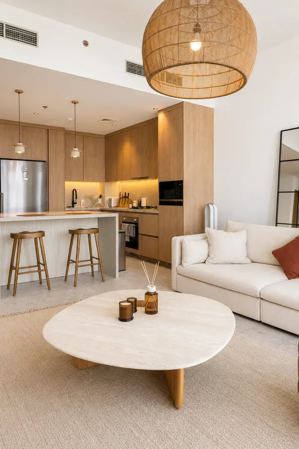 Warm minimalist open-plan apartment in Dubai with oak kitchen cabinetry, breakfast bar stools and a cream sofa