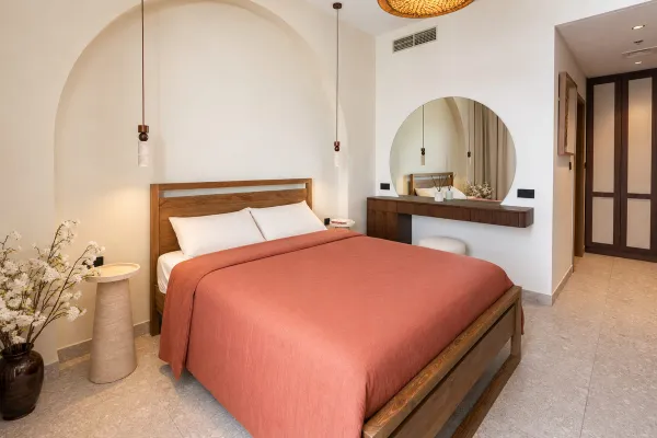 Warm minimalist bedroom in Dubai Hills with an arched plaster niche, oak bed frame and earthy terracotta tones
