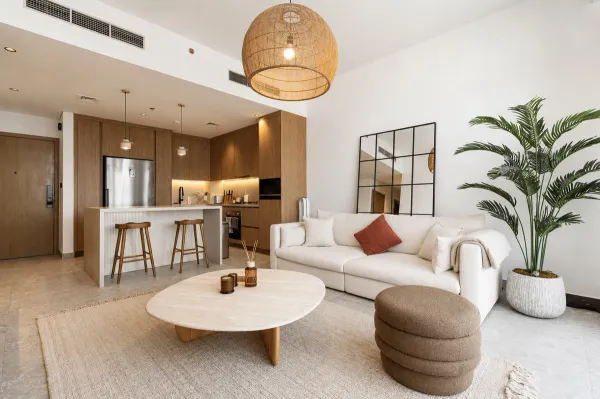 Modern Dubai apartment living room with a cream sofa, rattan pendant light, travertine coffee table and open-plan kitche