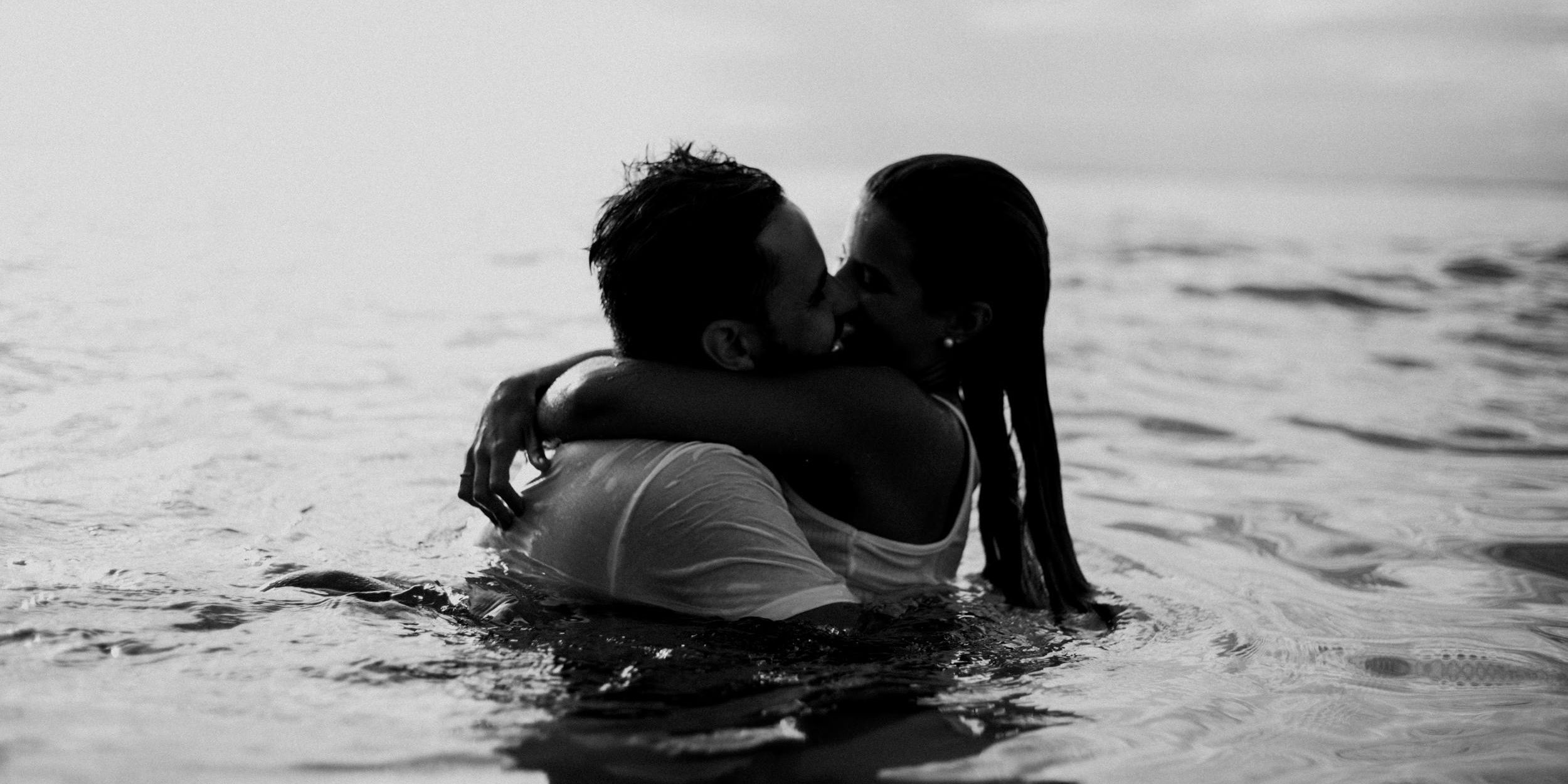 a man and a woman are kissing in the ocean .