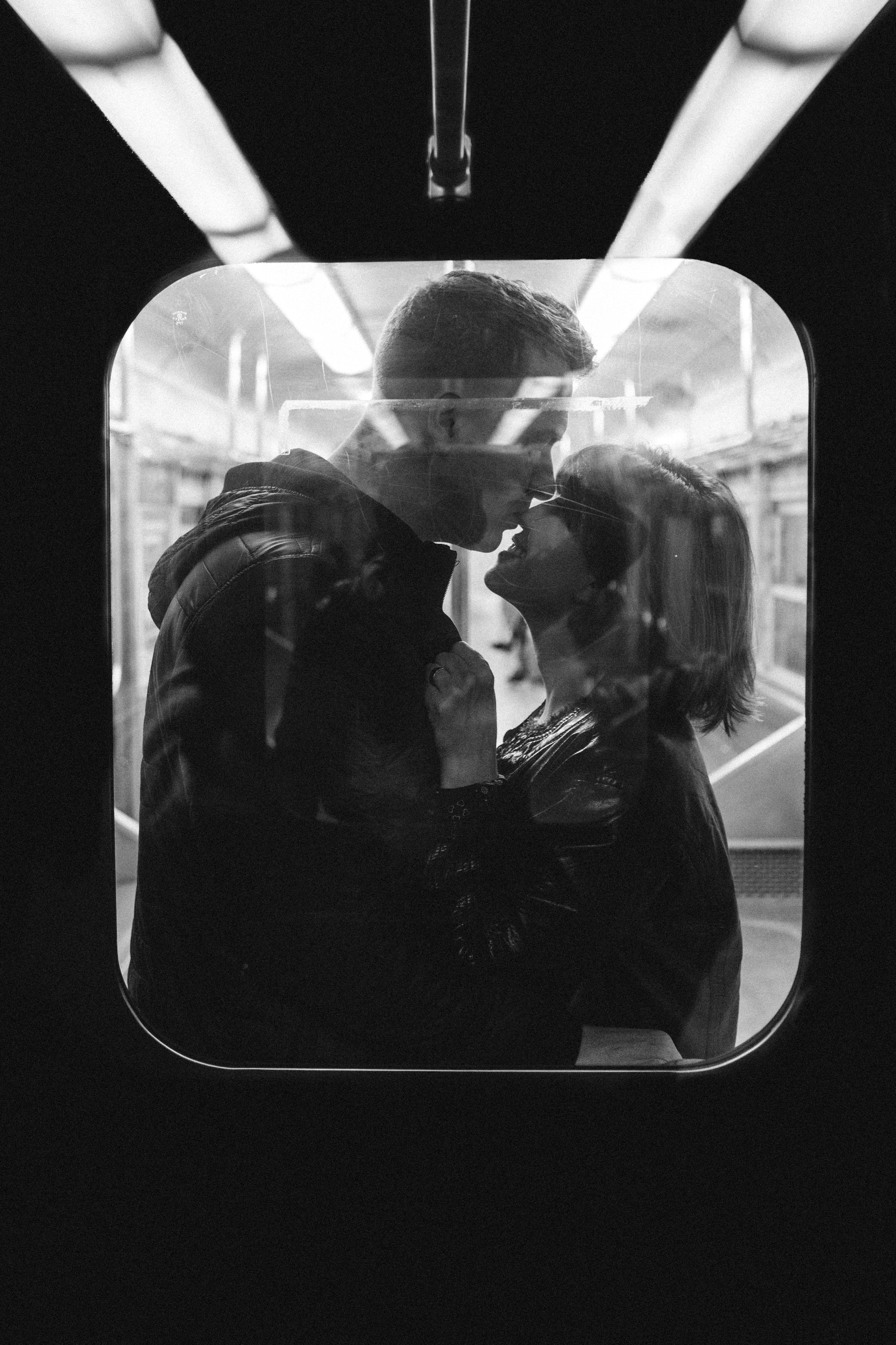 a black and white photo of a man and woman kissing on a train