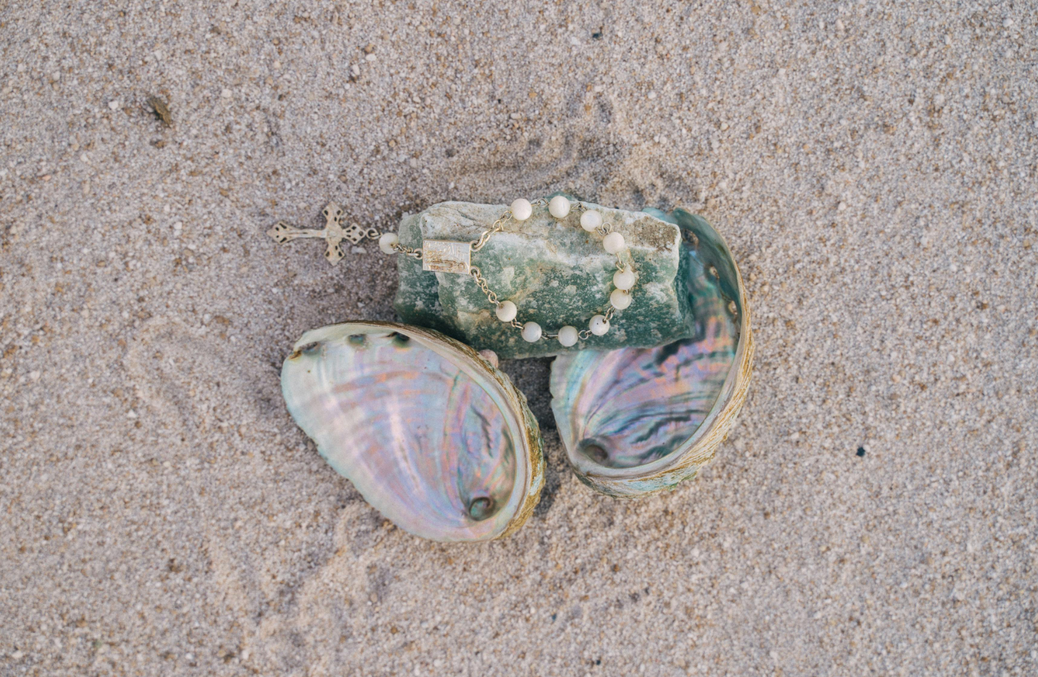 several shells are laying on the sand including one that has a cross on it
