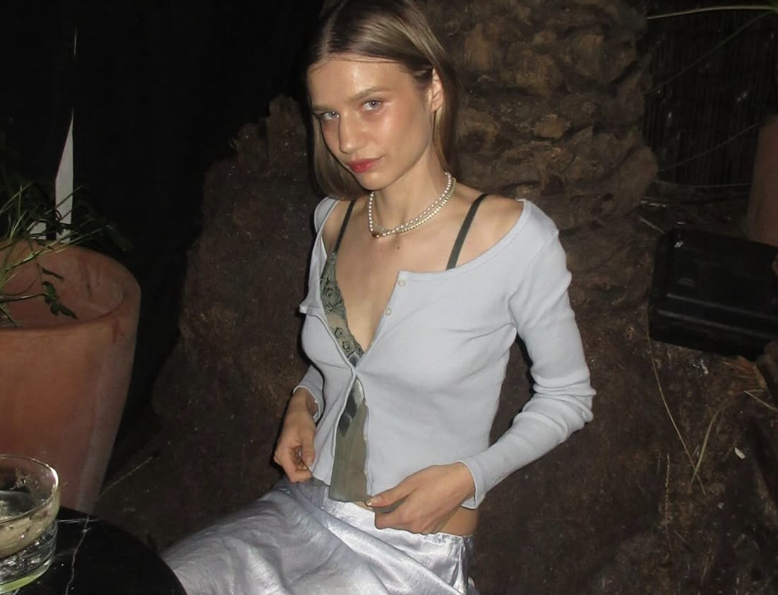 a woman wearing a pearl necklace is sitting in front of a potted plant