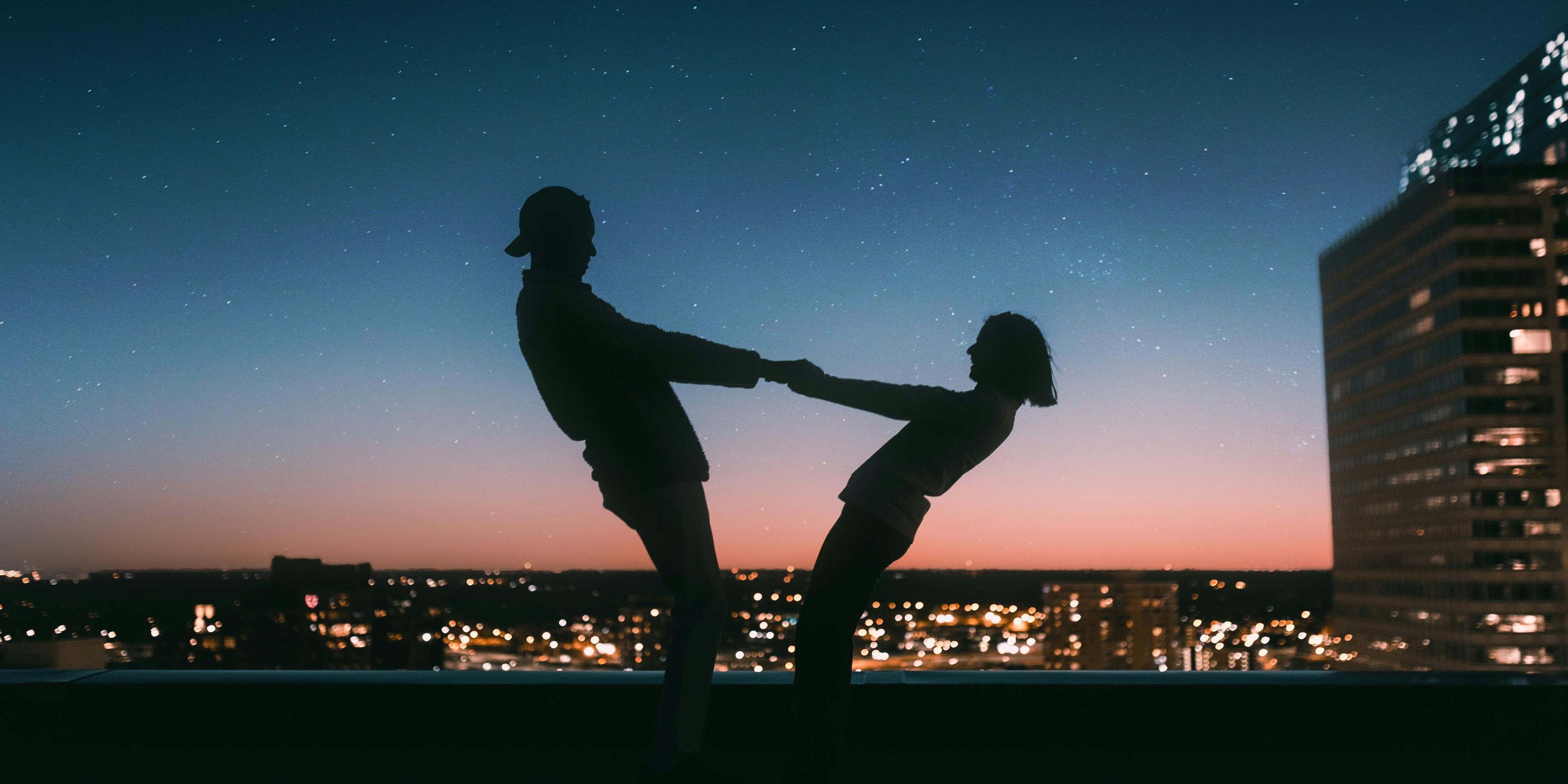 a man and a woman are dancing on a rooftop at night .