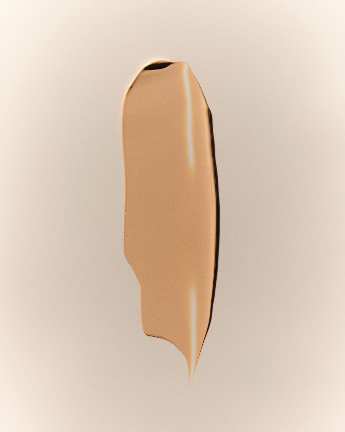 Foundation texture swatch: a smooth, creamy vertical swipe of warm golden-beige foundation with soft highlights on a neutral background