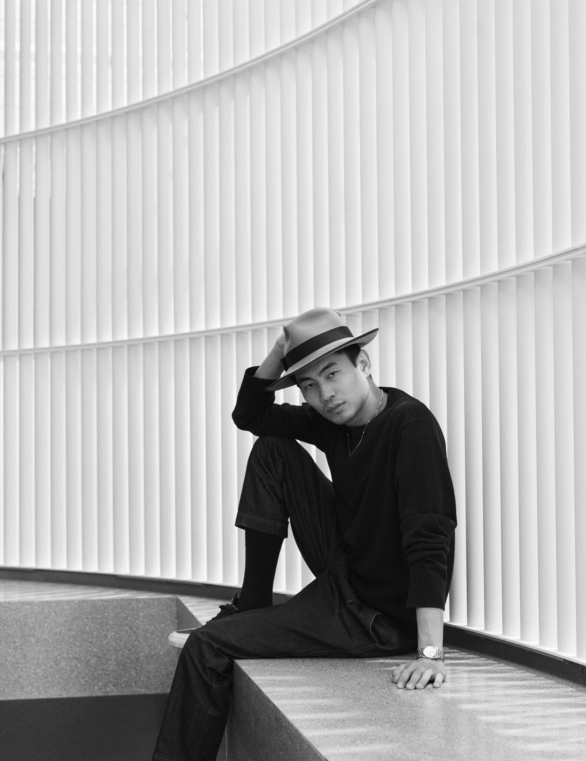 Black-and-white portrait of Han Zhoug, founder of Mr Selfportrait, seated in dark clothes and a brimmed hat inside his first London store.