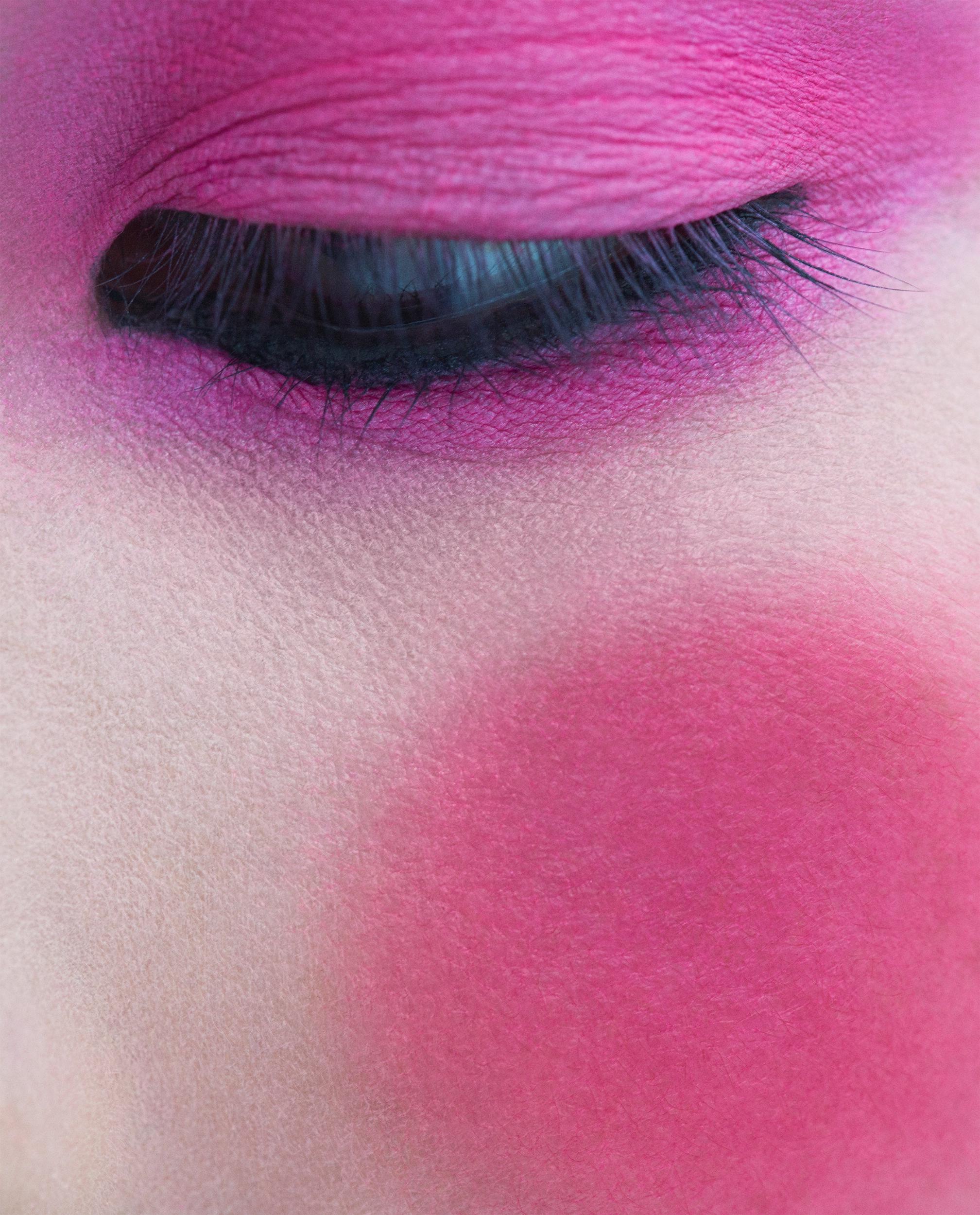 Extreme close-up of a closed eye with vivid magenta eyeshadow, black liner and lashes, and a matching bold pink blush smudged across the cheek.