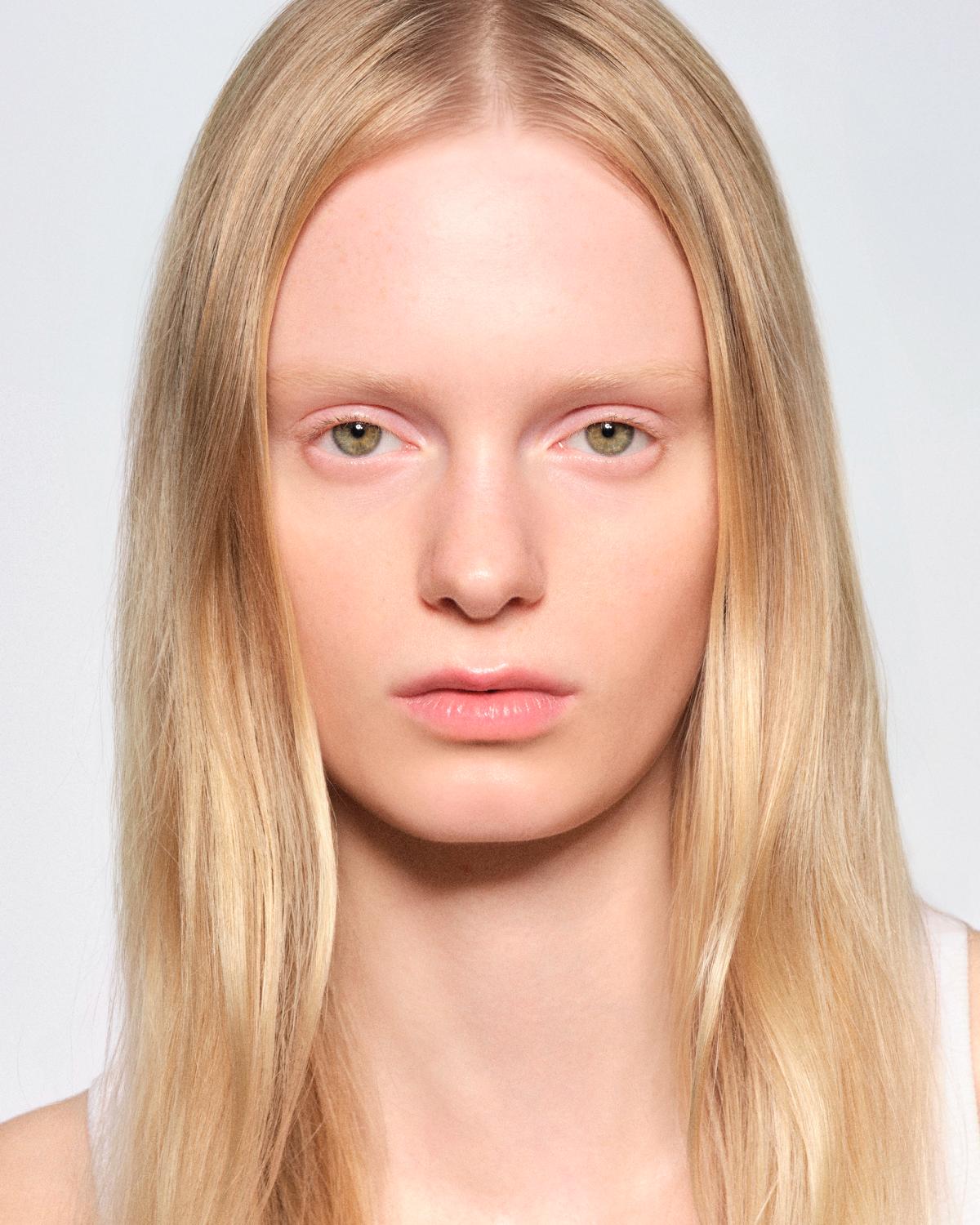Portrait of a woman with long, straight blonde hair parted in the center, green eyes, pale pink lids, and a natural look.