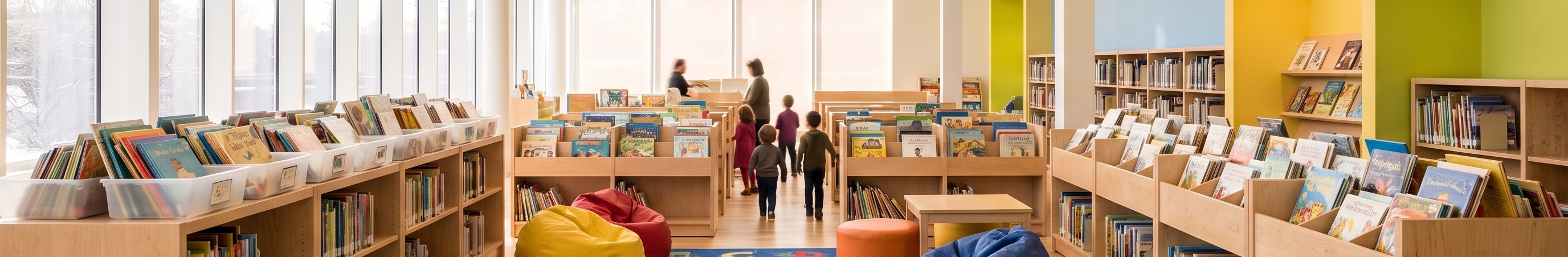 A children’s library with low colourful shelving, picture-book bins and soft seating, figures browsing in the background.