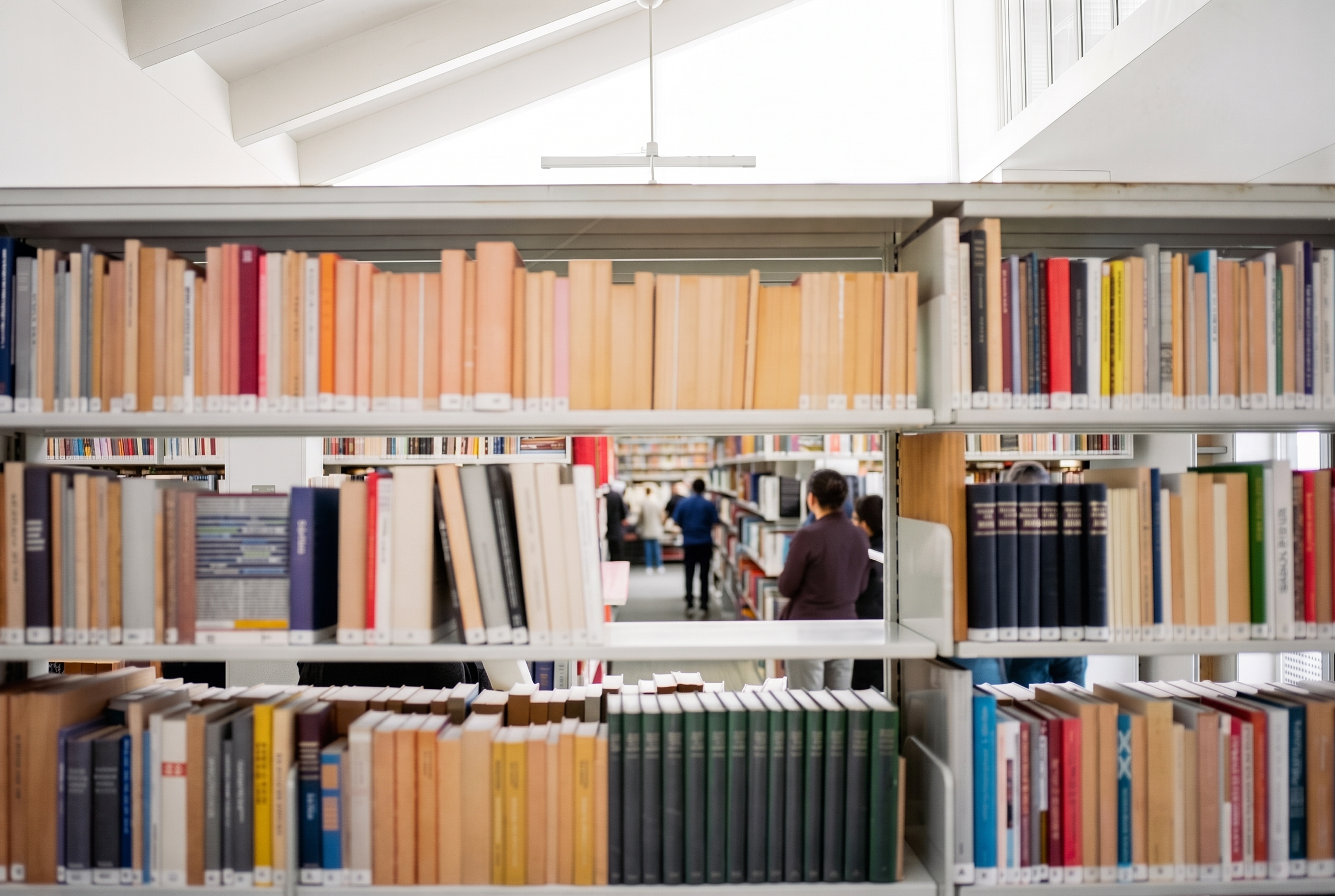 A public library reading area in use, visitors browsing and reading among the shelves.