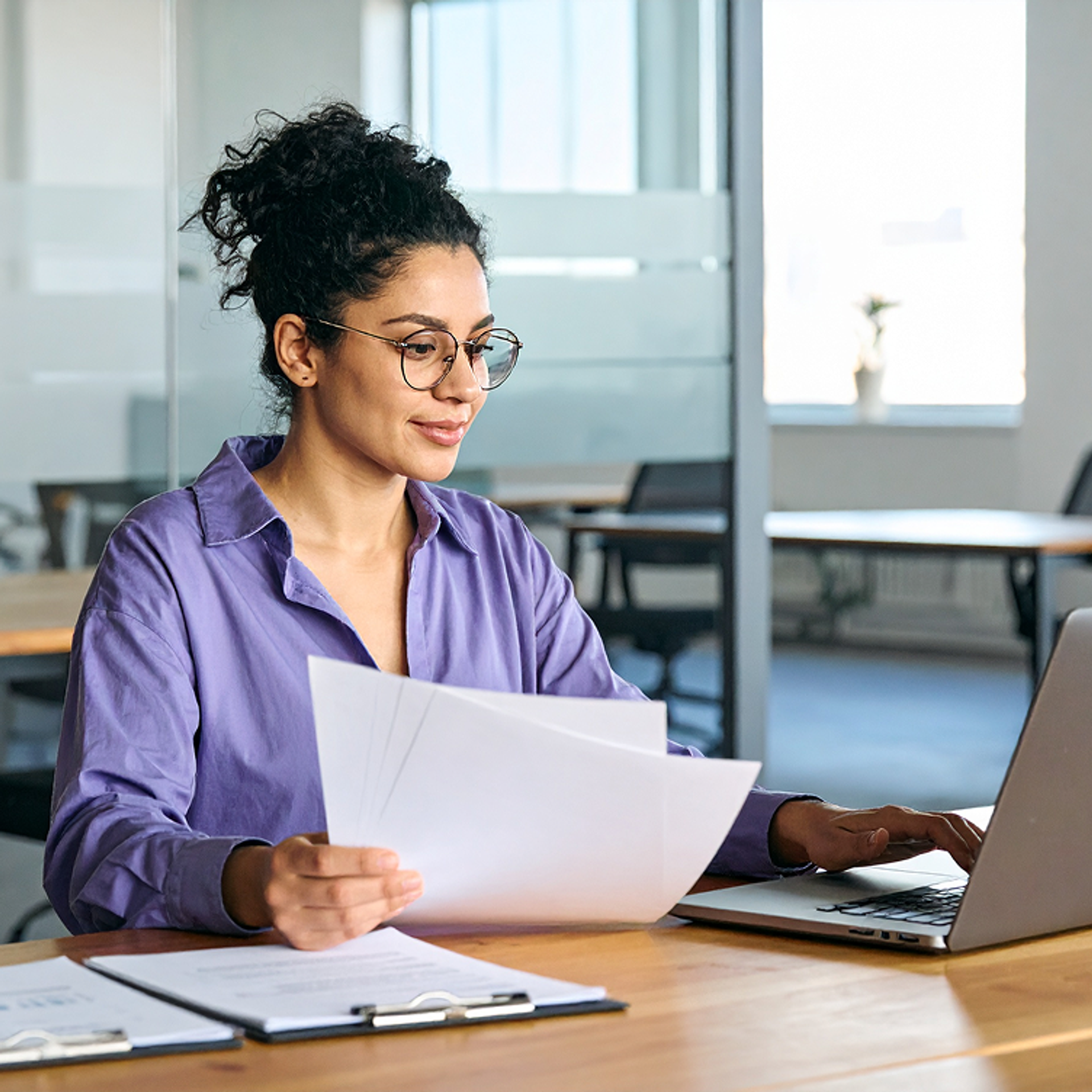 Woman works at a desk with papers and a laptop