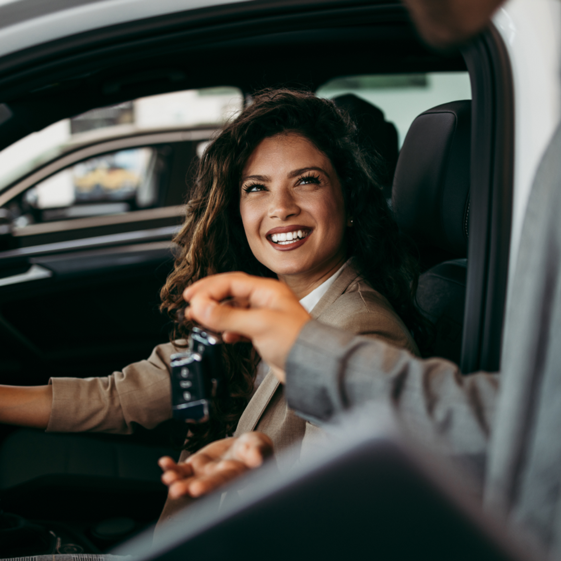 A woman sitting inside her new car. A salesman is giving her the car's keys.