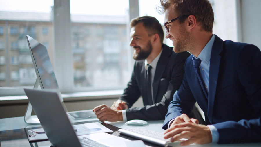 Two business man working on their laptops and smiling.