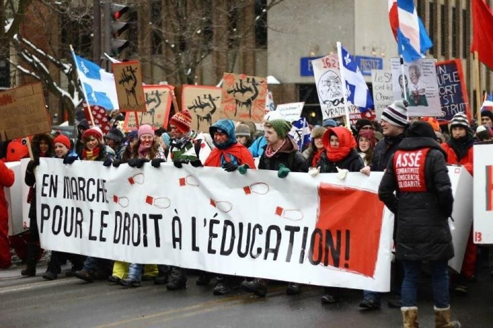 Students in winter hats and red scarves march in the snow behind a banner reading "En marche pour le droit à l'éducation!", with Québec flags and raised-fist placards behind them.