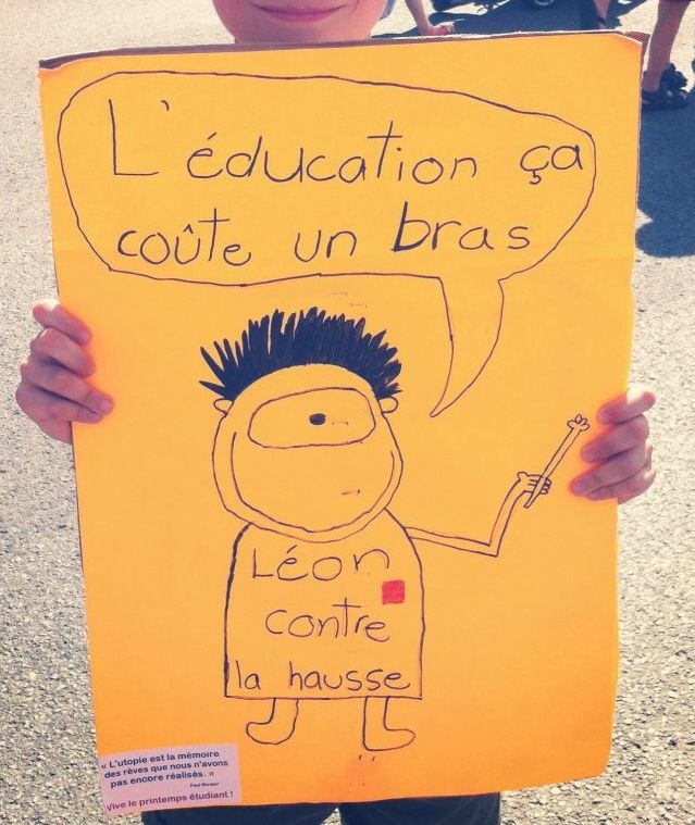 A child holds up an orange hand-drawn poster of a one-eyed cartoon figure wearing a red square, with a speech bubble reading "L'éducation ça coûte un bras" and the words "Léon contre la hausse."