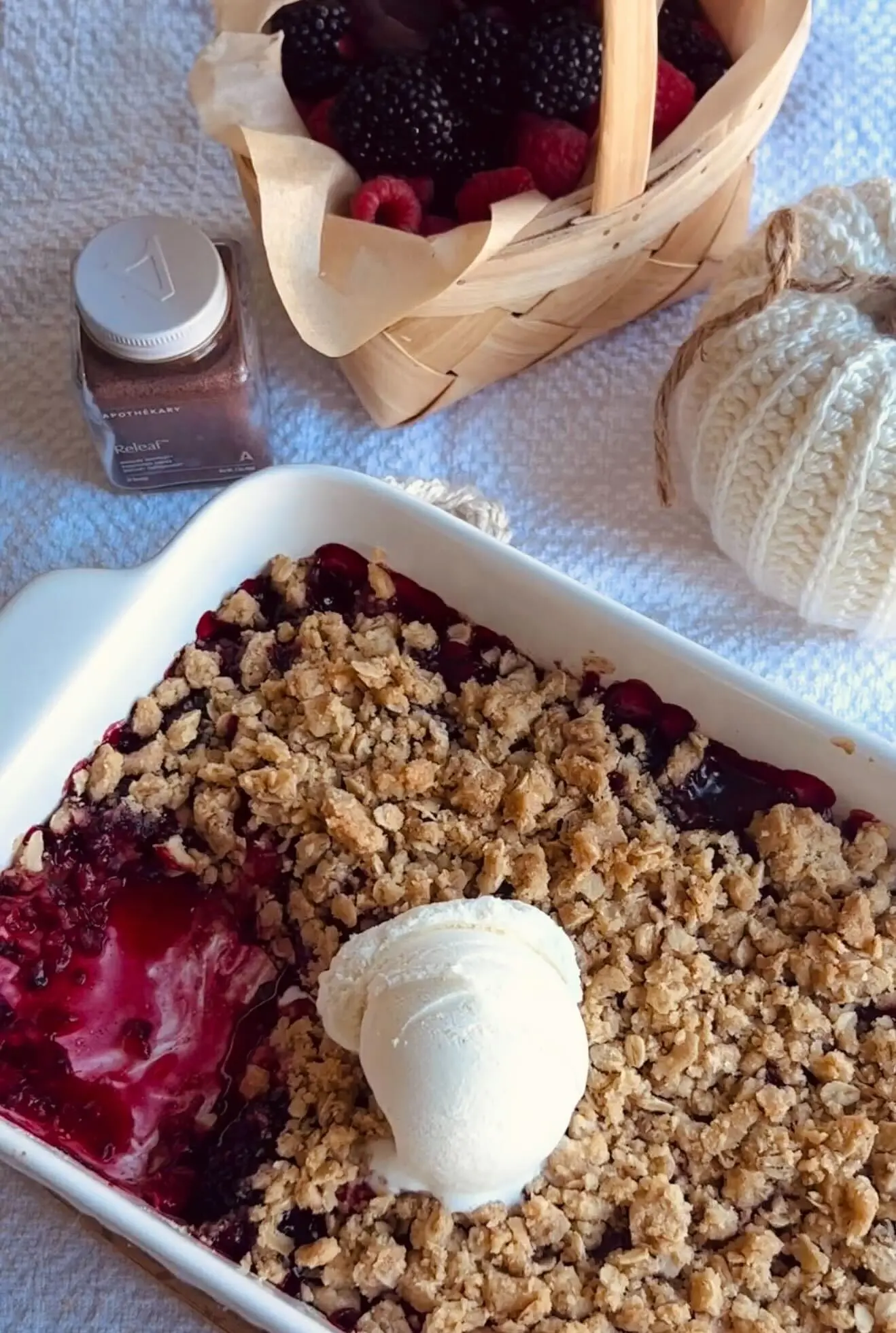 Berry crumble dessert in a baking dish with scoop of it taken out and a scoop of vanilla ice cream on top