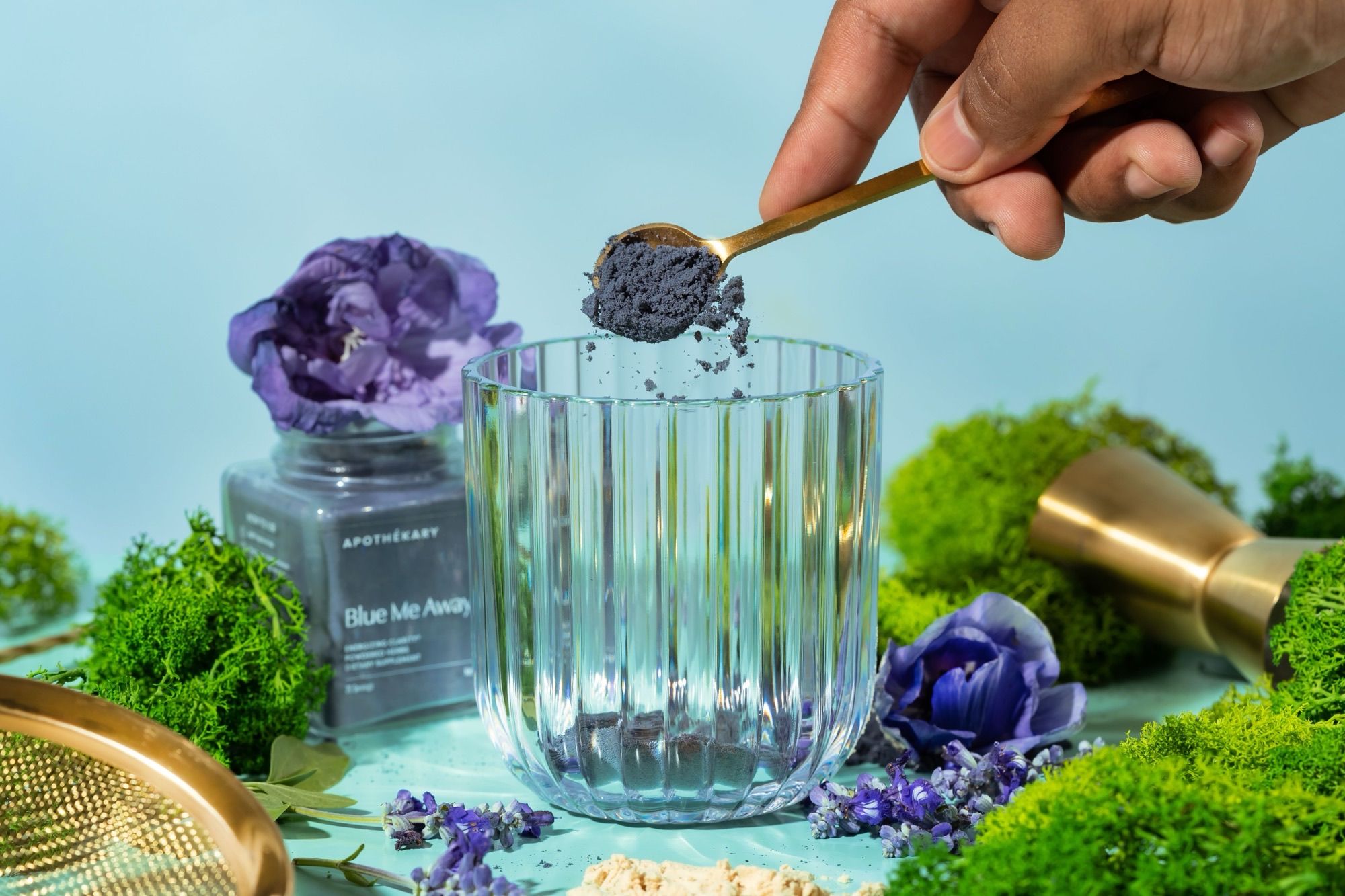 herbs being scooped into a clear glass surrounded by greenery