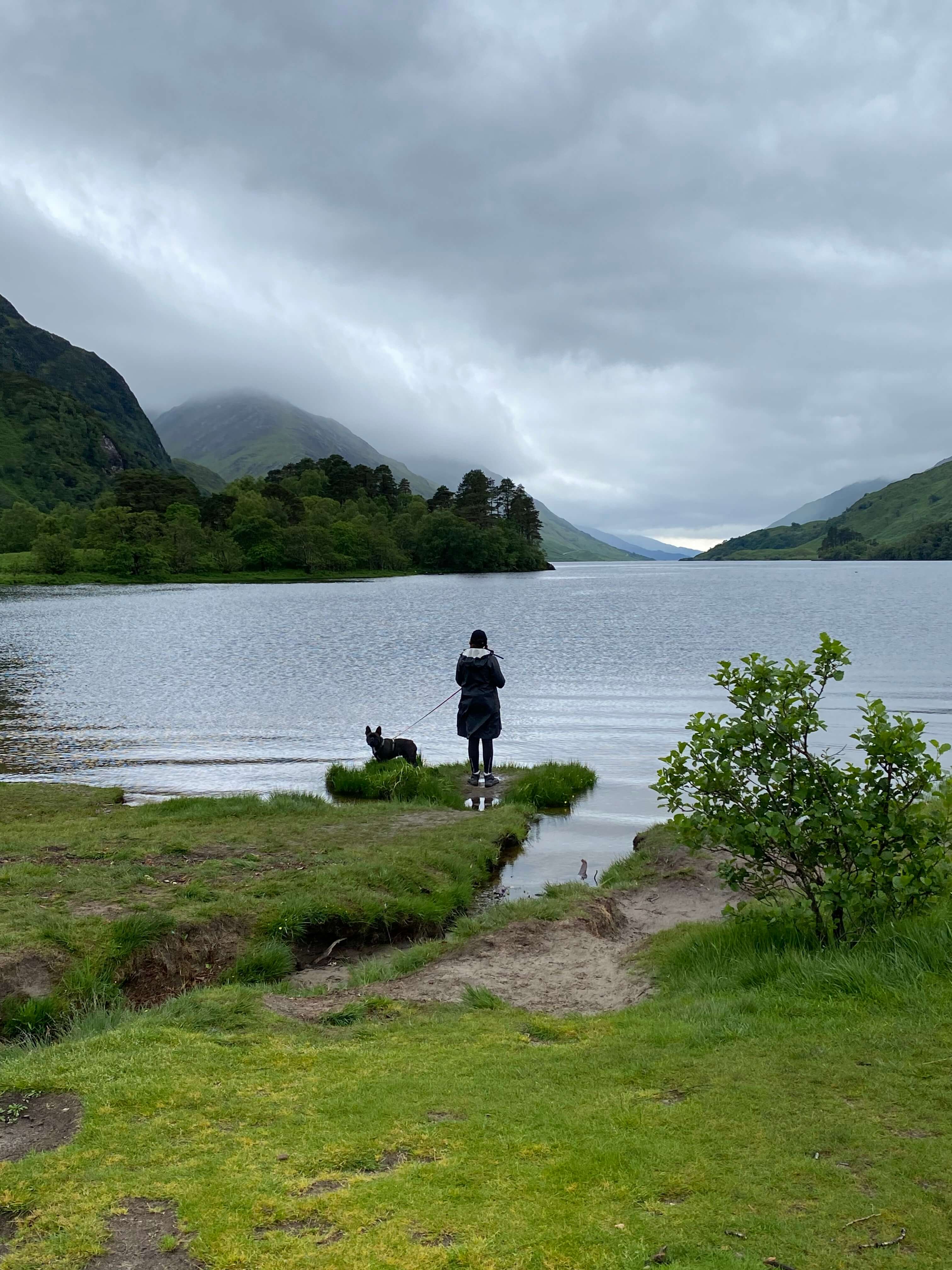 Person and dog standing at the shores of a lake in the Highlands